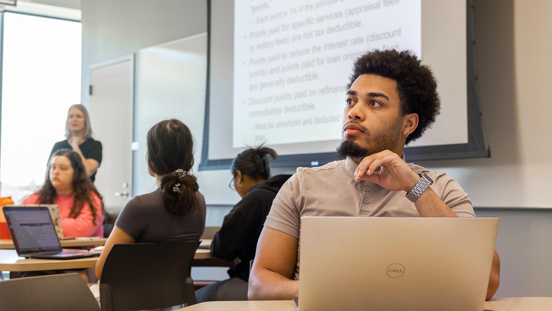 A person sitting at a table in a classroom with a laptop.