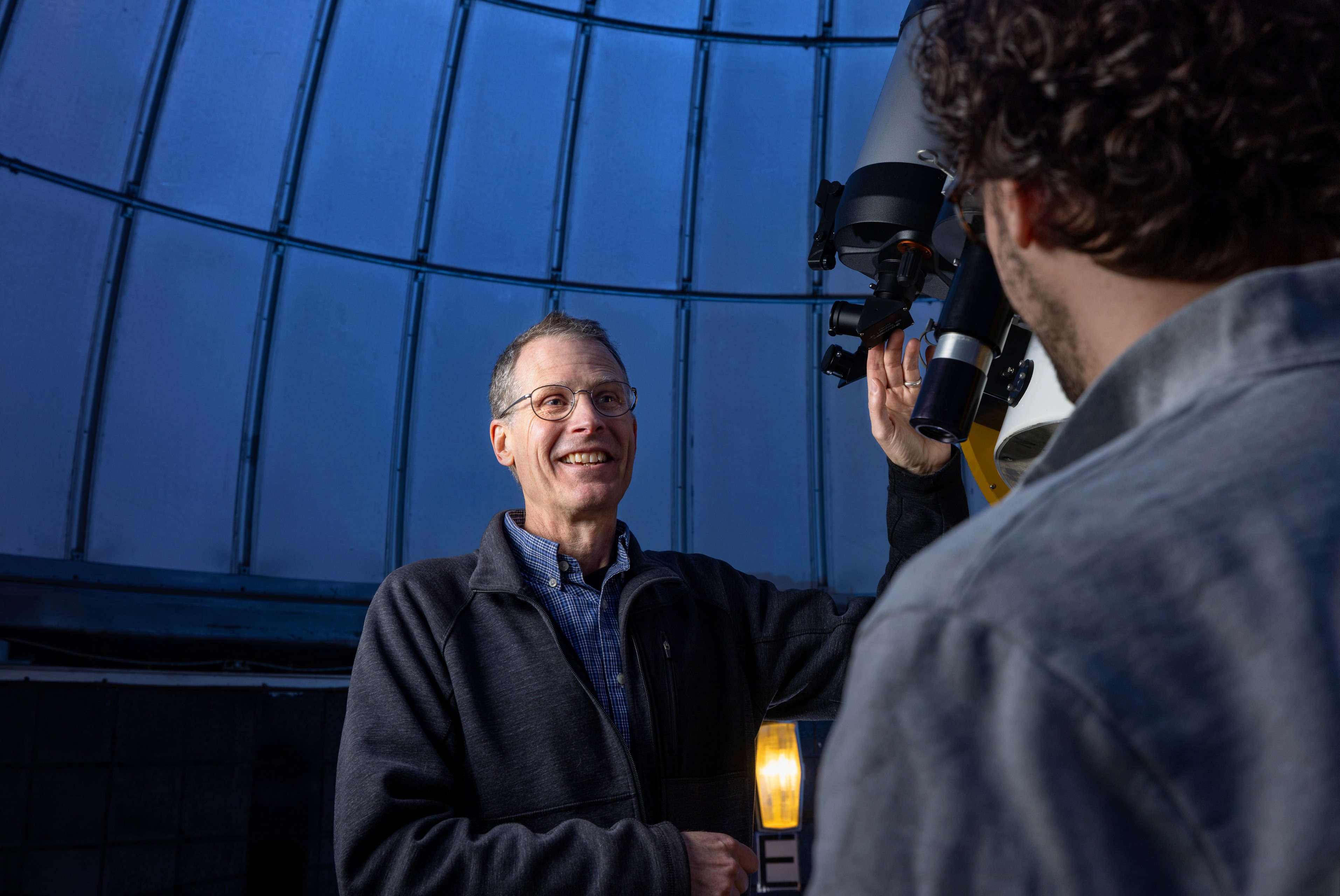 Dr. Andrew Layden speaks to a student in front of a telescope.