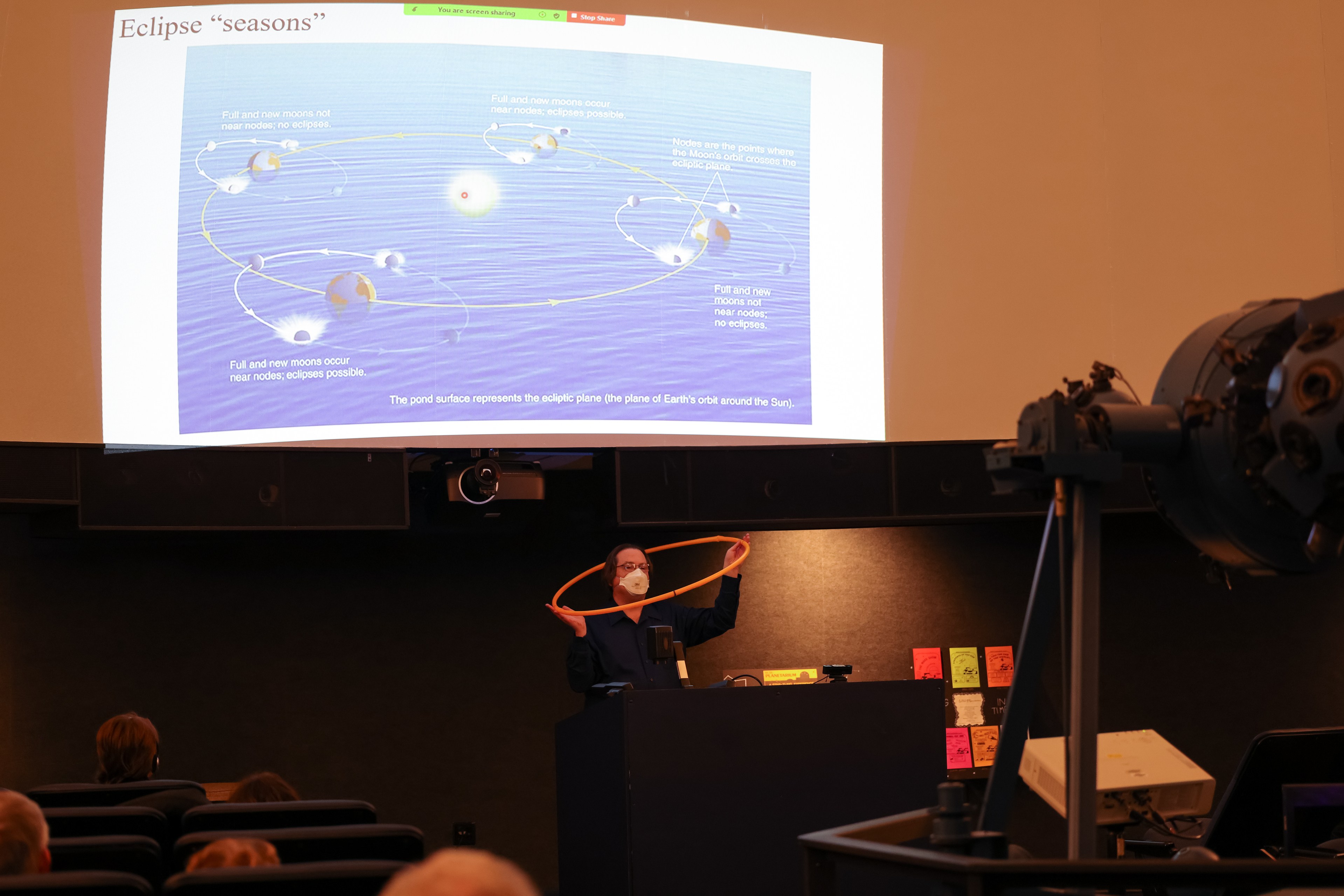 A man stands in front of a screen with a slide reading "Eclipse Seasons."