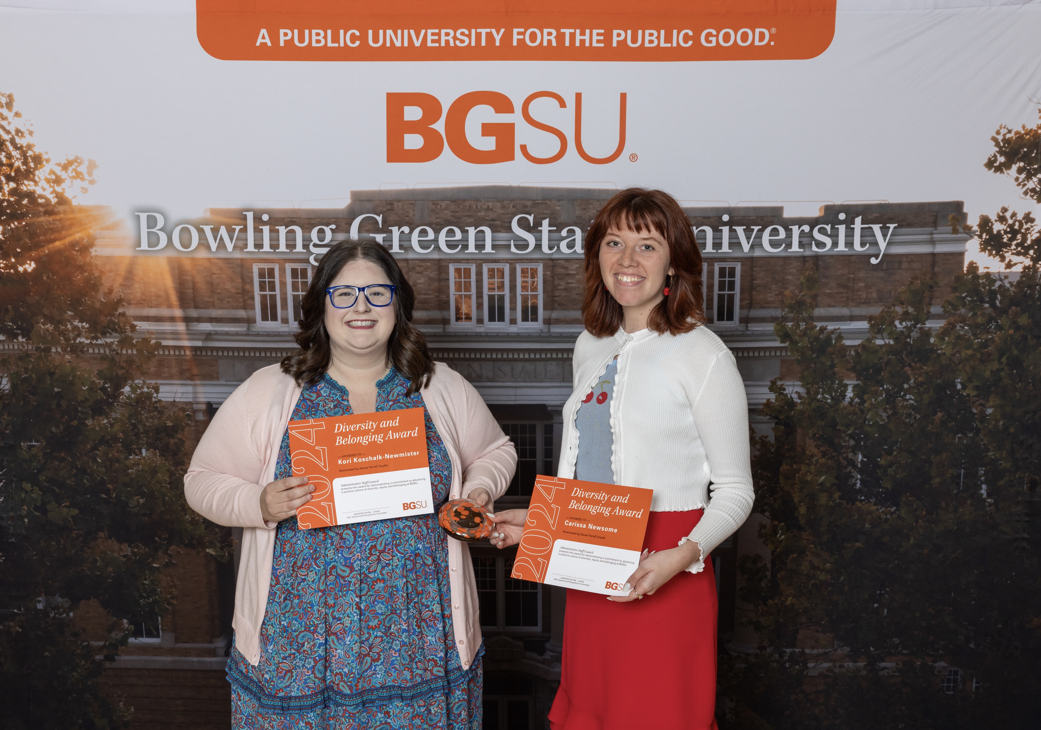 Two women hold orange award certificates 