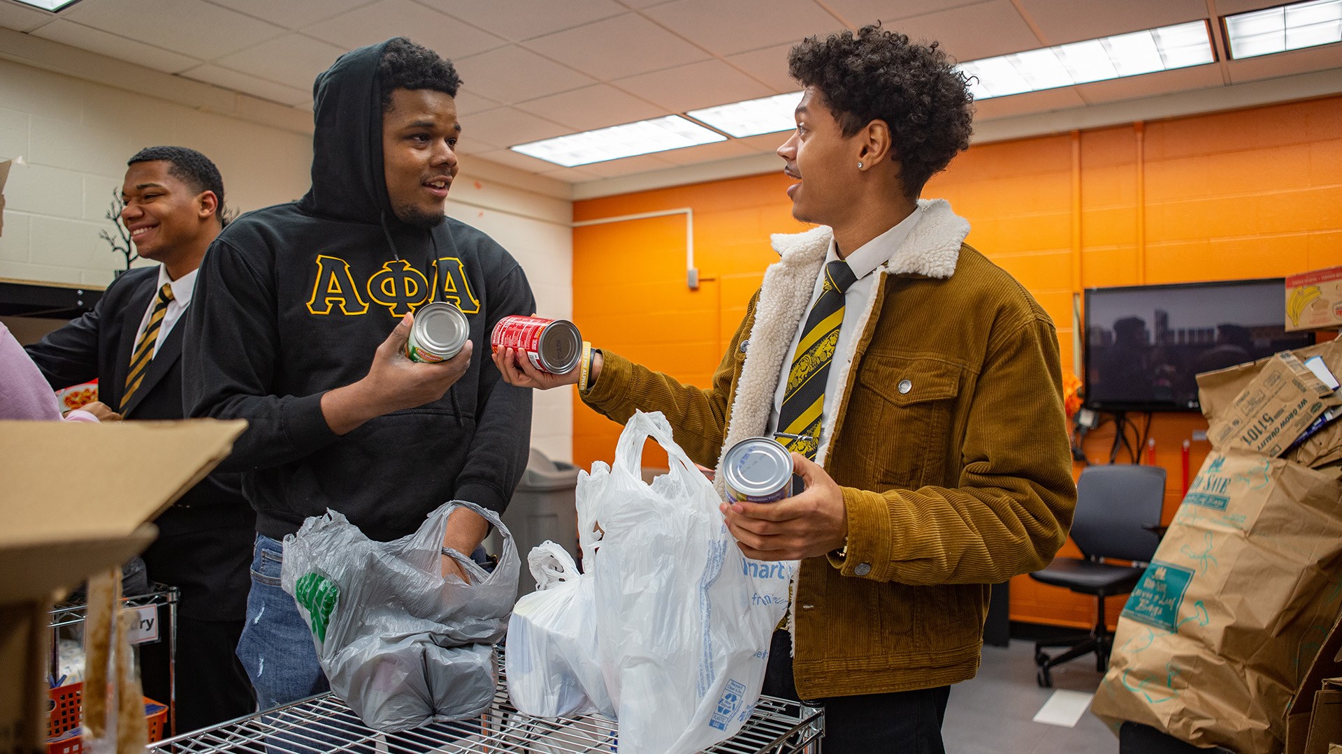 Two people empty bags of canned food to fill the shelves at a food pantry.