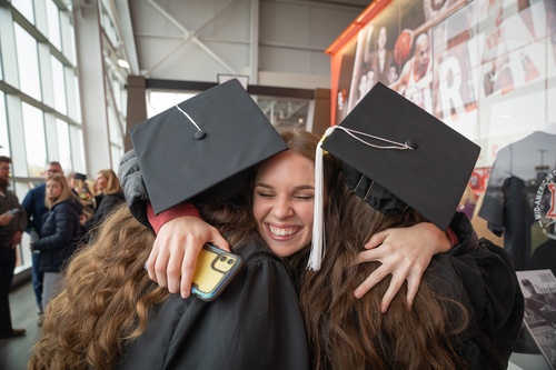 An individual hugs two graduating students at commencment
