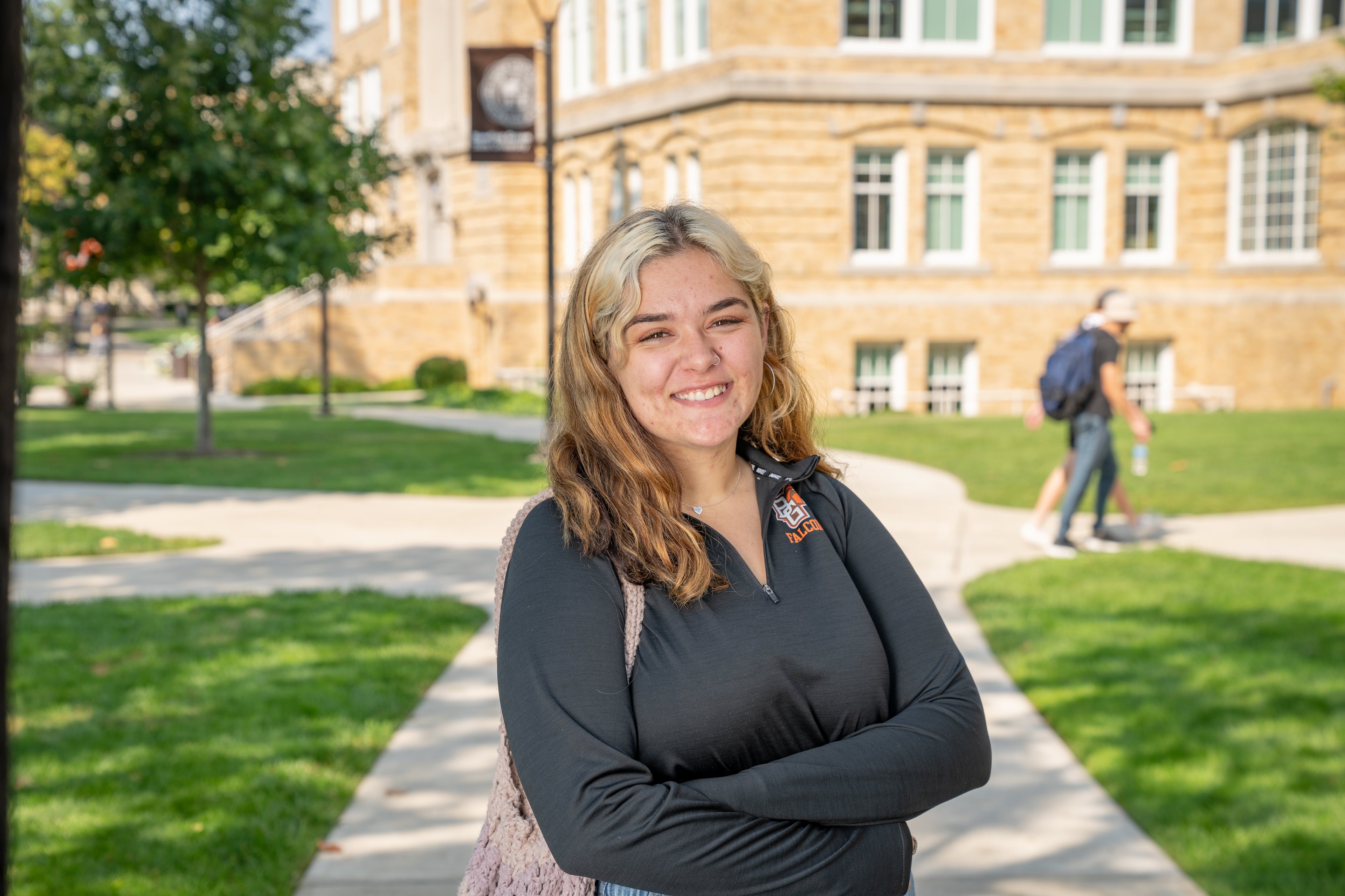 Student Kaylee stands outside at BGSU on a sunny day wearing a grey BGSU quarter zip sweatshirt