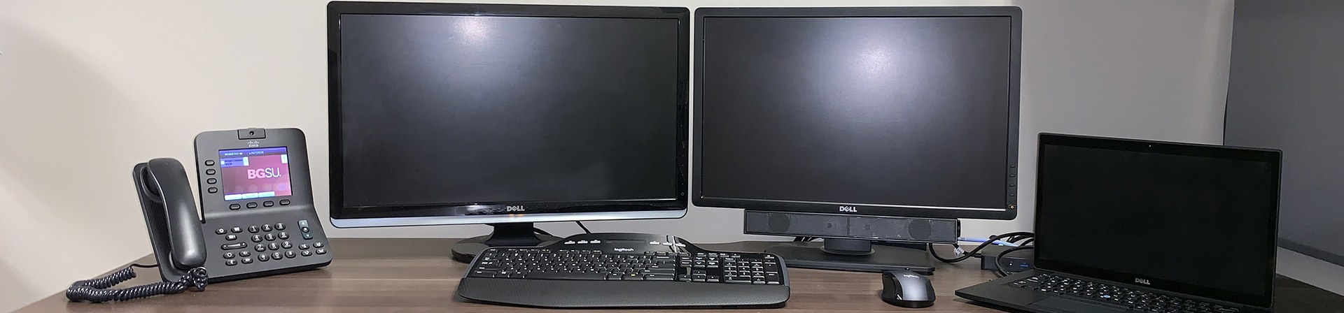 desk setup with university phone, two monitors a dell laptop and a wireless keyboard and mouse