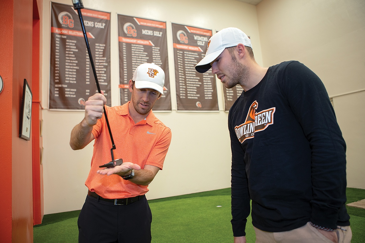 John Powers holding a golf club and explaining it to a student-athlete