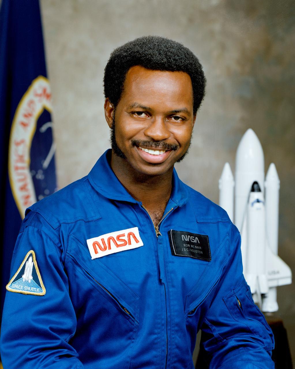 Dr. Ronald E. McNair seated in a NASA suit in front of a model of a space shuttle
