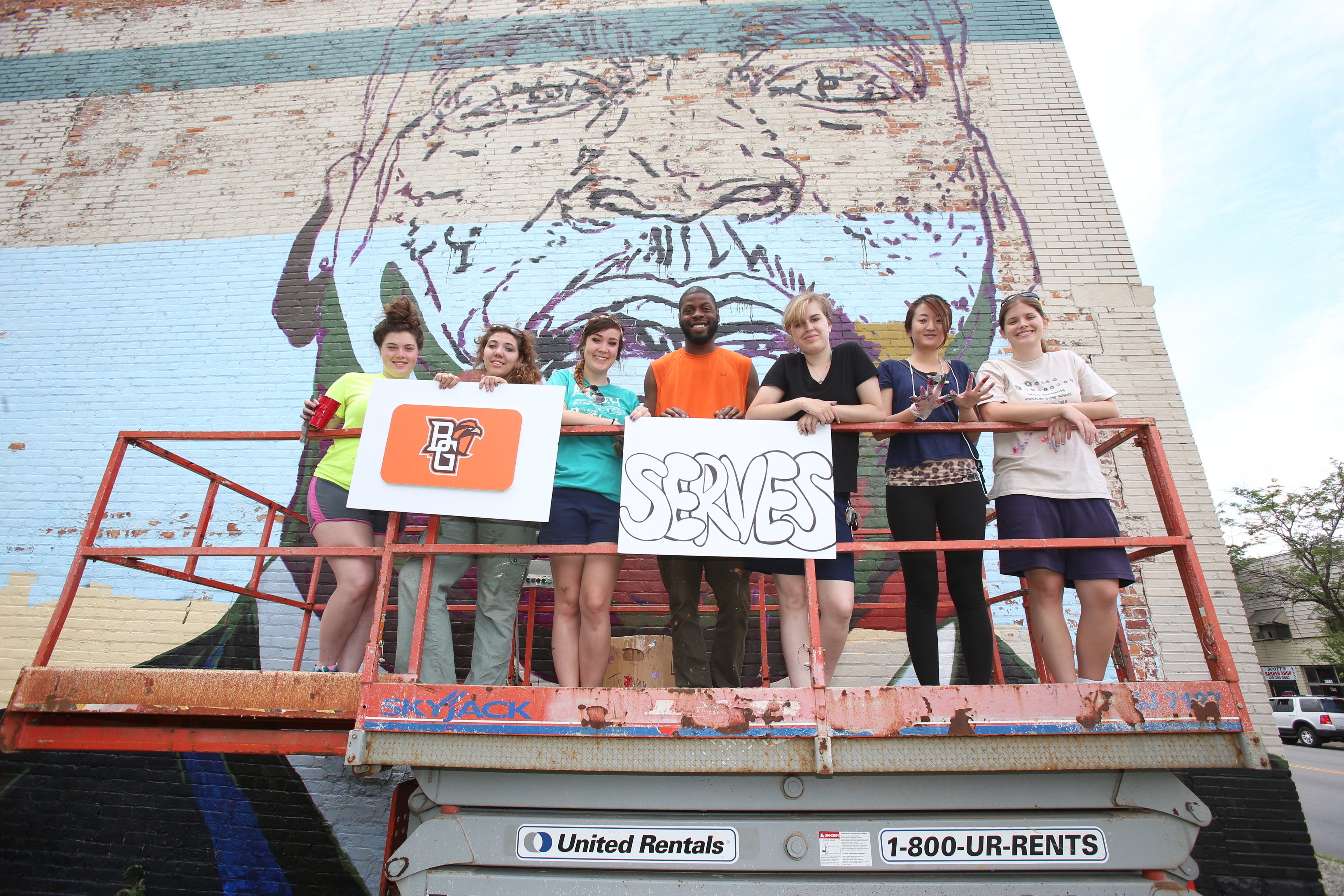 BGSU MA in art education students pose on a scissor lift in front of a mural, one of several in the northwest Ohio area that our students worked on.