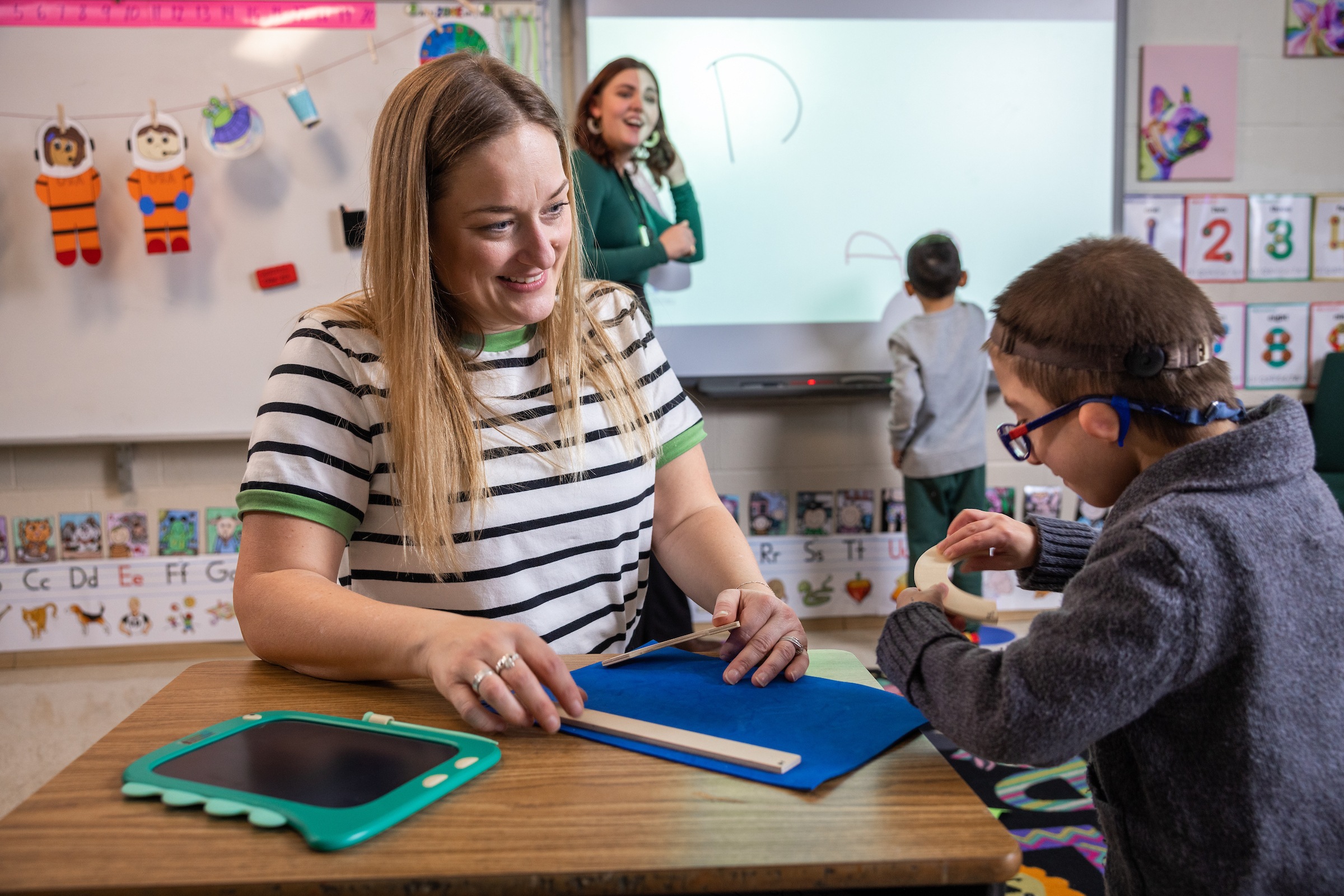 An teacher sits with a mother and little girl in a classroom