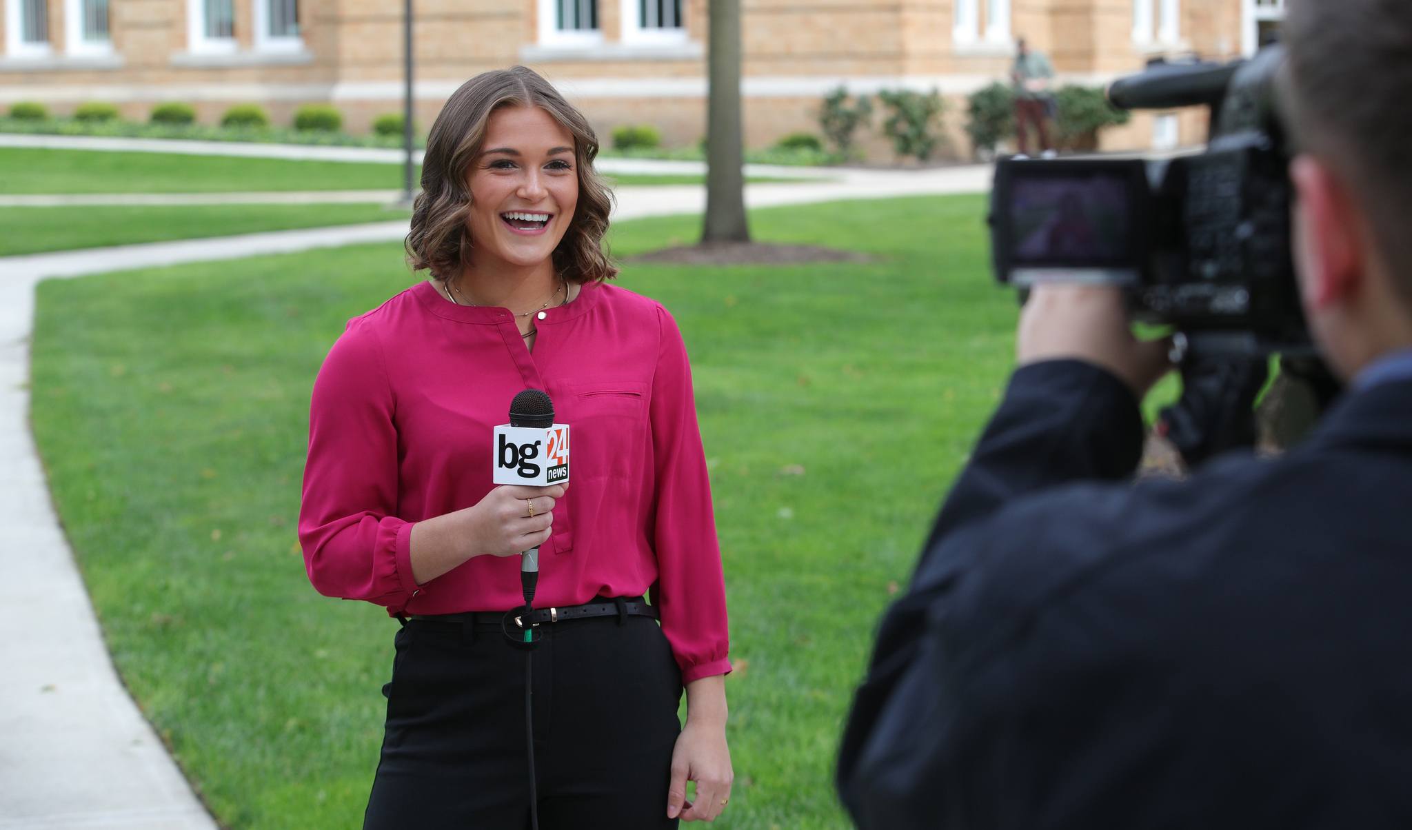 Journalism student holds a microphone while being filmed near the Bowen Thompson Union