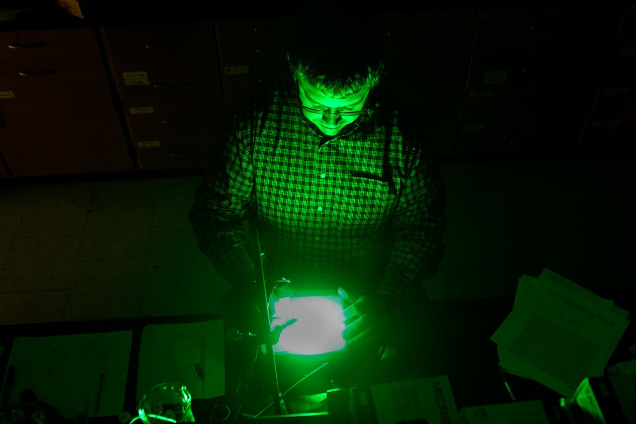 Dr. Joe Furgal stands over a bright green light as part of his experiments to understand the interaction of light and matter, with the BGSU Ph.D. in Photochemical Sciences