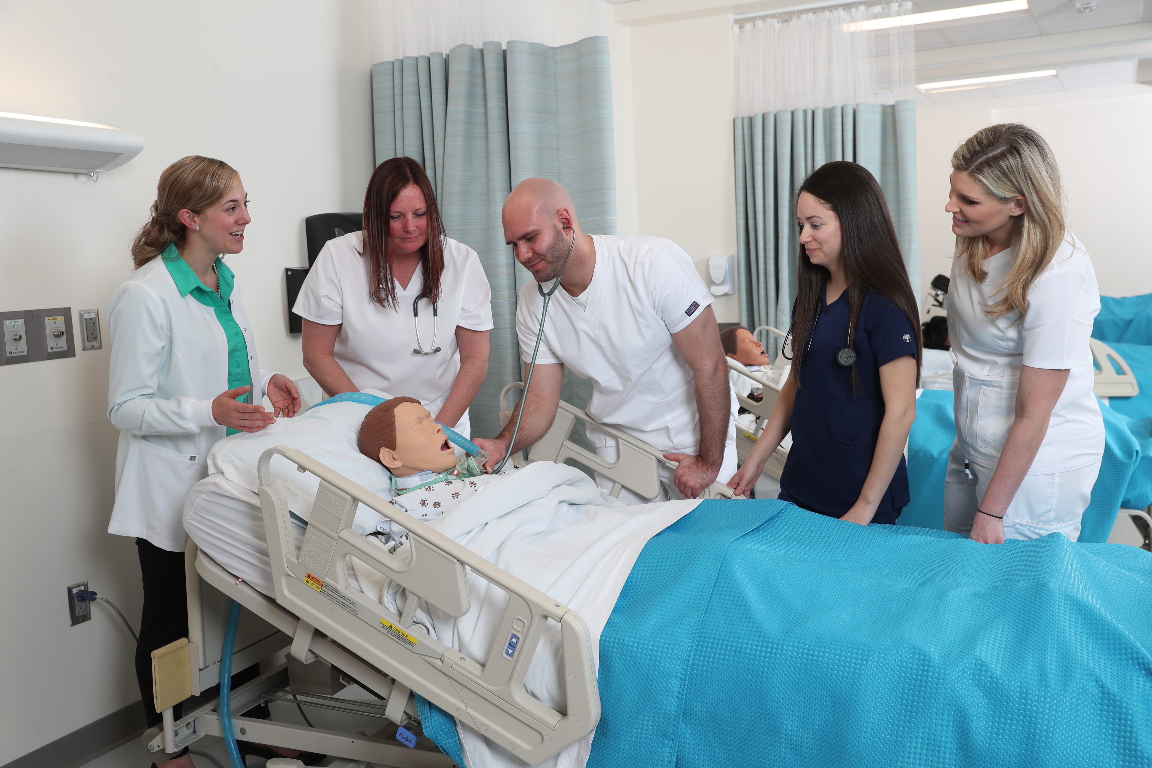Four BGSU BSN students take the heartbeat of a simulation mannequin with a professor looking on in an Ohio classroom.