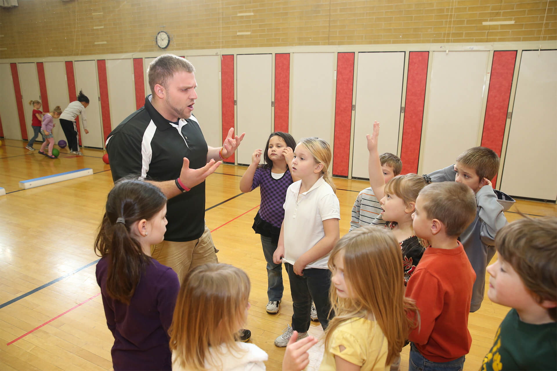 A physical education teacher talks to a group of kids in a gymnasium