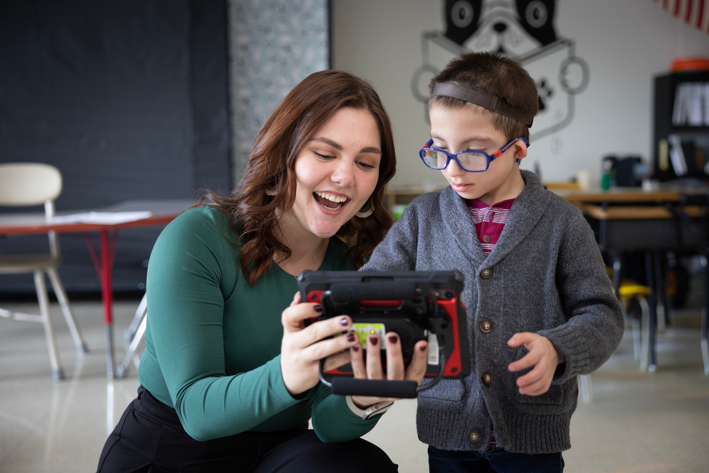 A female assistive technology master’s student helps a child with disabilities use a computer.