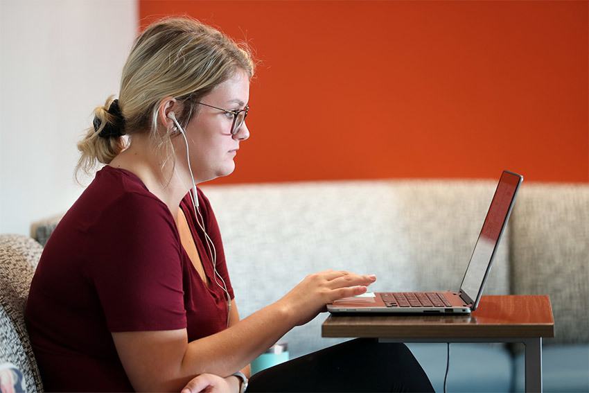 Young student studying on laptop with earbuds in ears