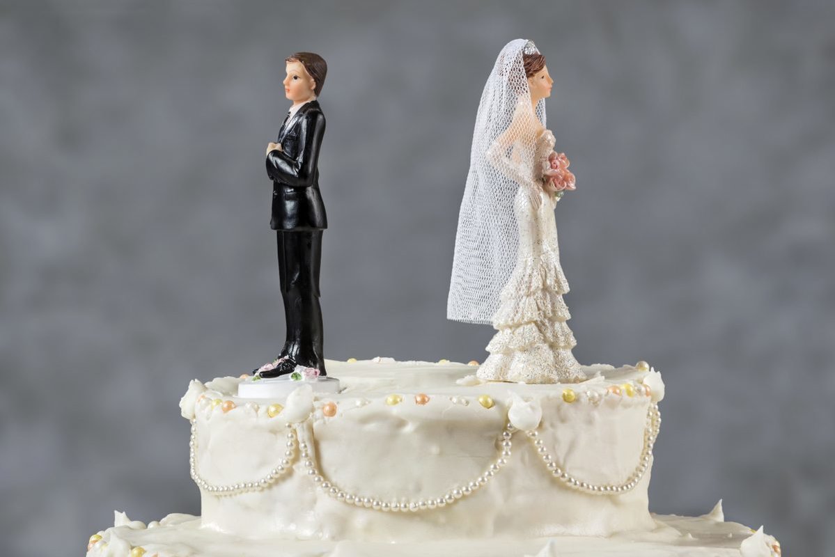 Couple on top of wedding cake with large gap between them and backs to one another