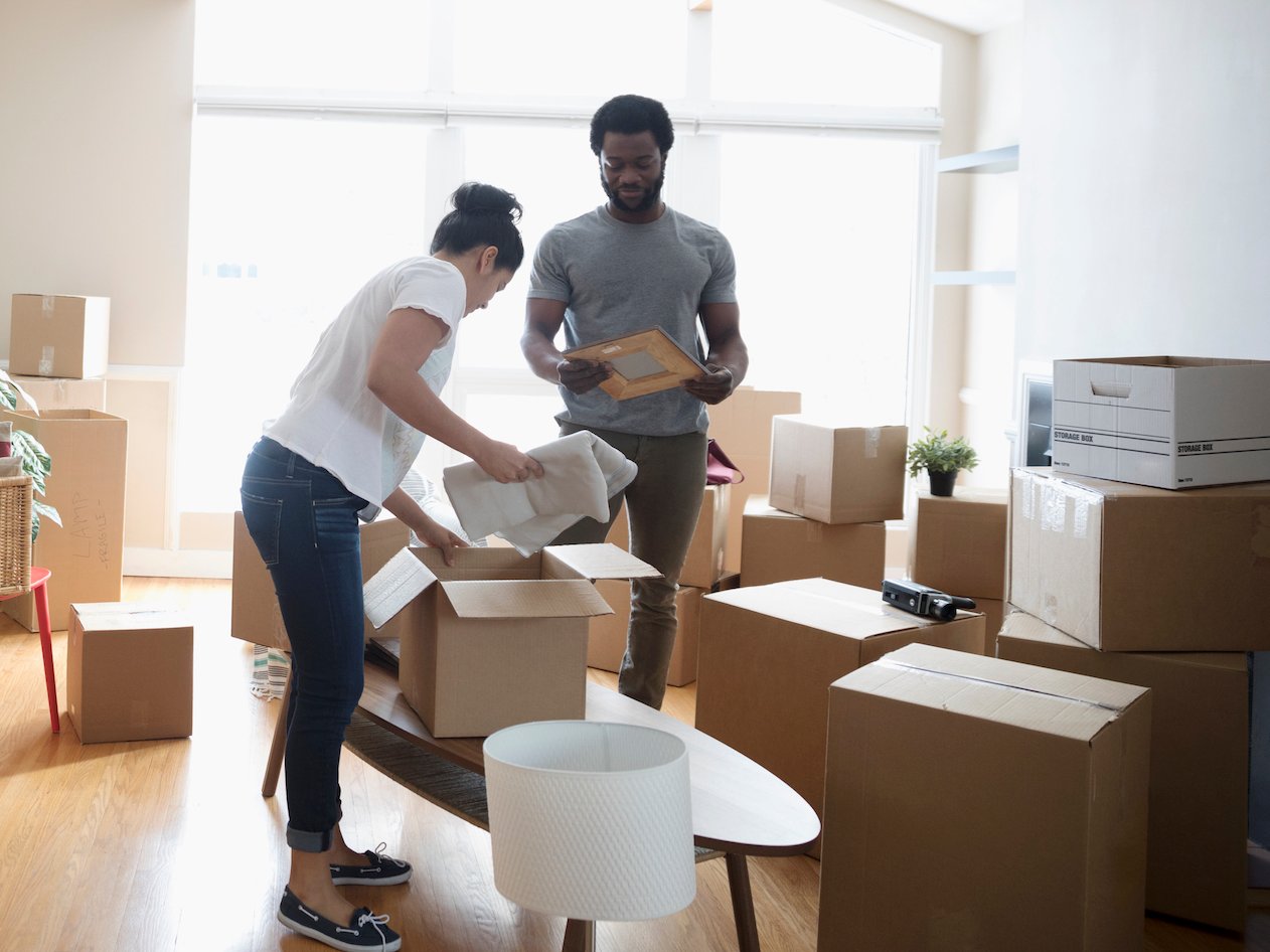 Image of young white woman and black man unpacking boxes in sparse living space