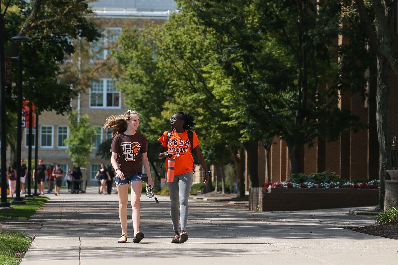 Two students walking the tree-lined BGSU Ohio campus. Pre-mortuary science track students study anatomy and psychology here.