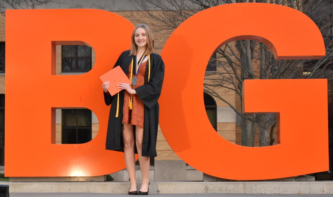 Emma Crawn in graduation gown in front of BG letters