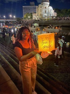 Student Briyanna stands in from of a crod along a river in Japan holding a lantern in honor of the Hiroshima bombing victims