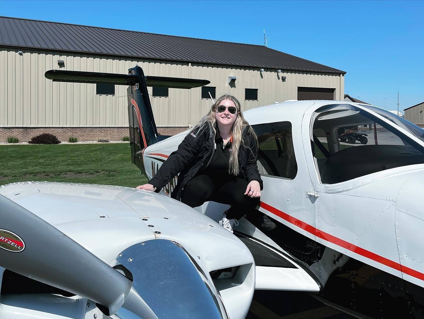 Student Lizz is dressed in all black and crouches on the wing of a single-engine BGSU airplane