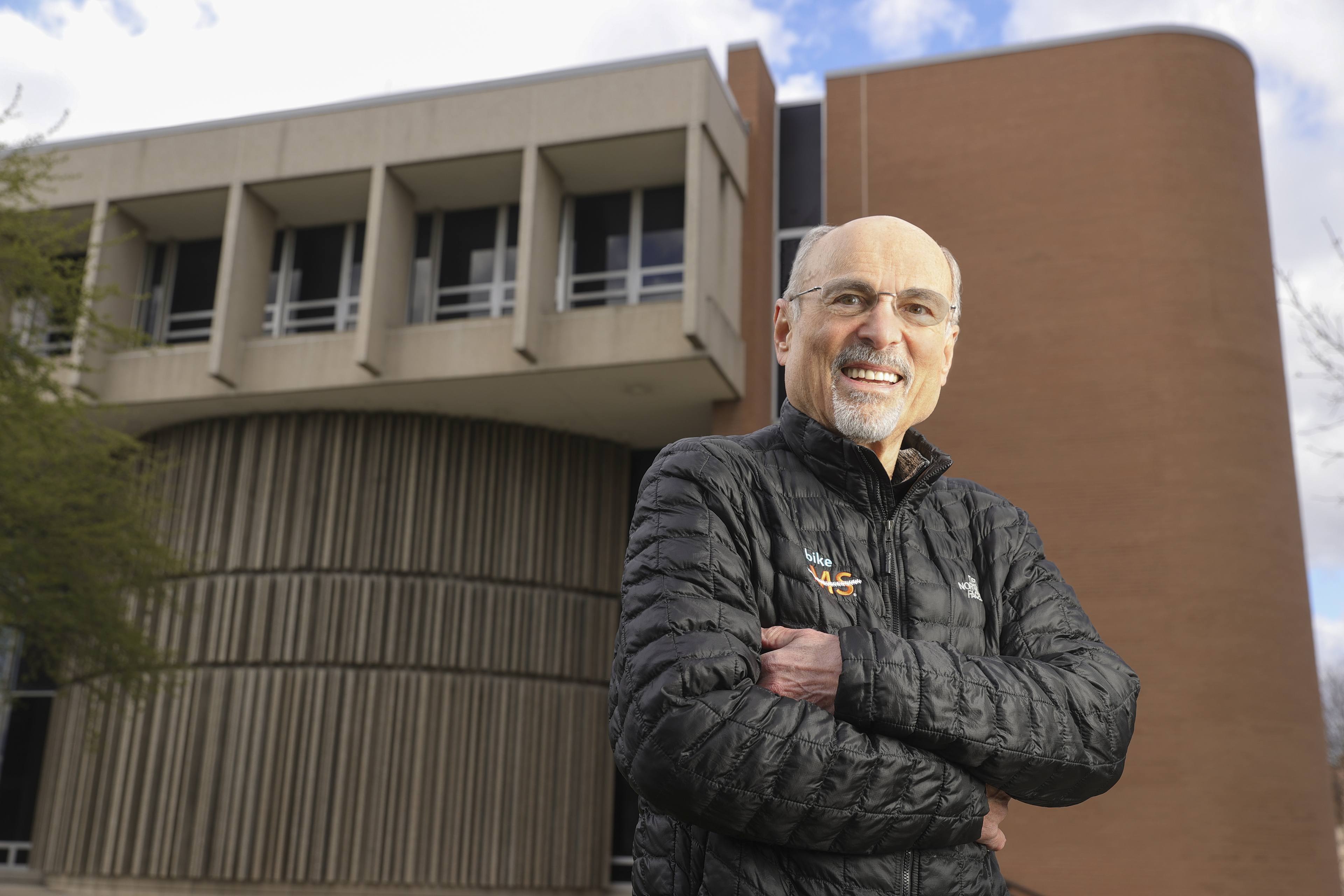 Geoff Radbill smiling with his arms crossed while standing in front of the Math and Science Building on BGSU Campus
