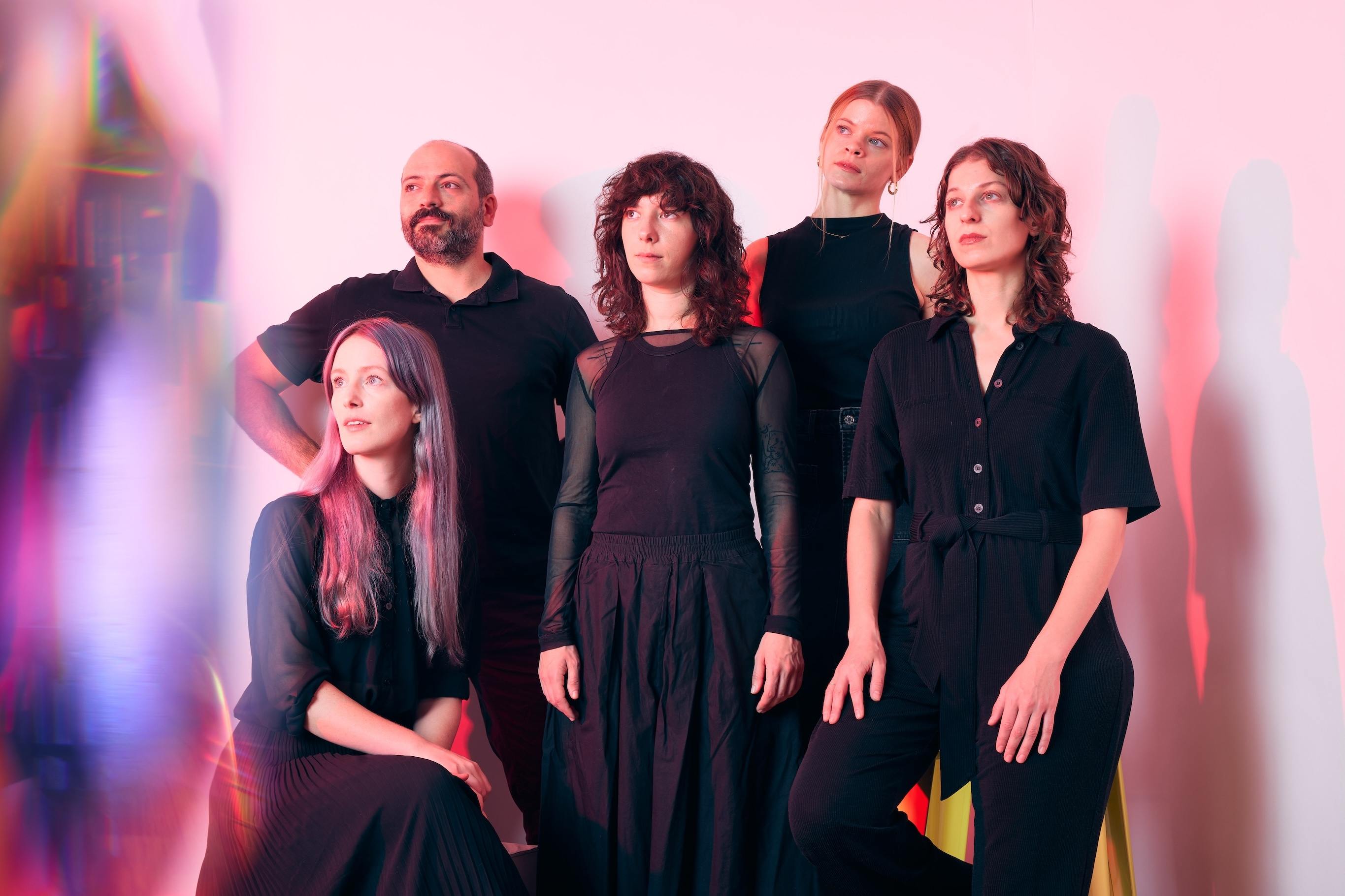 TAK Ensemble posing against a wall, with pink lights pointed at them