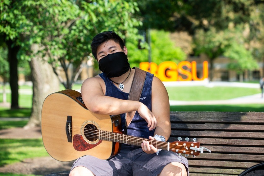 Student playing guitar outside on campus
