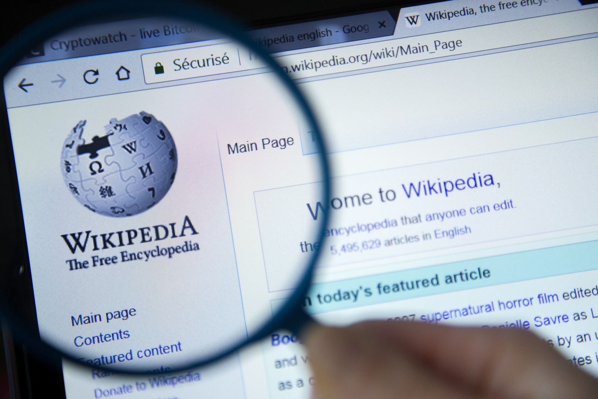 Wikipedia homepage on the computer screen under magnifying glass. Wikipedia is a free Internet encyclopedia.