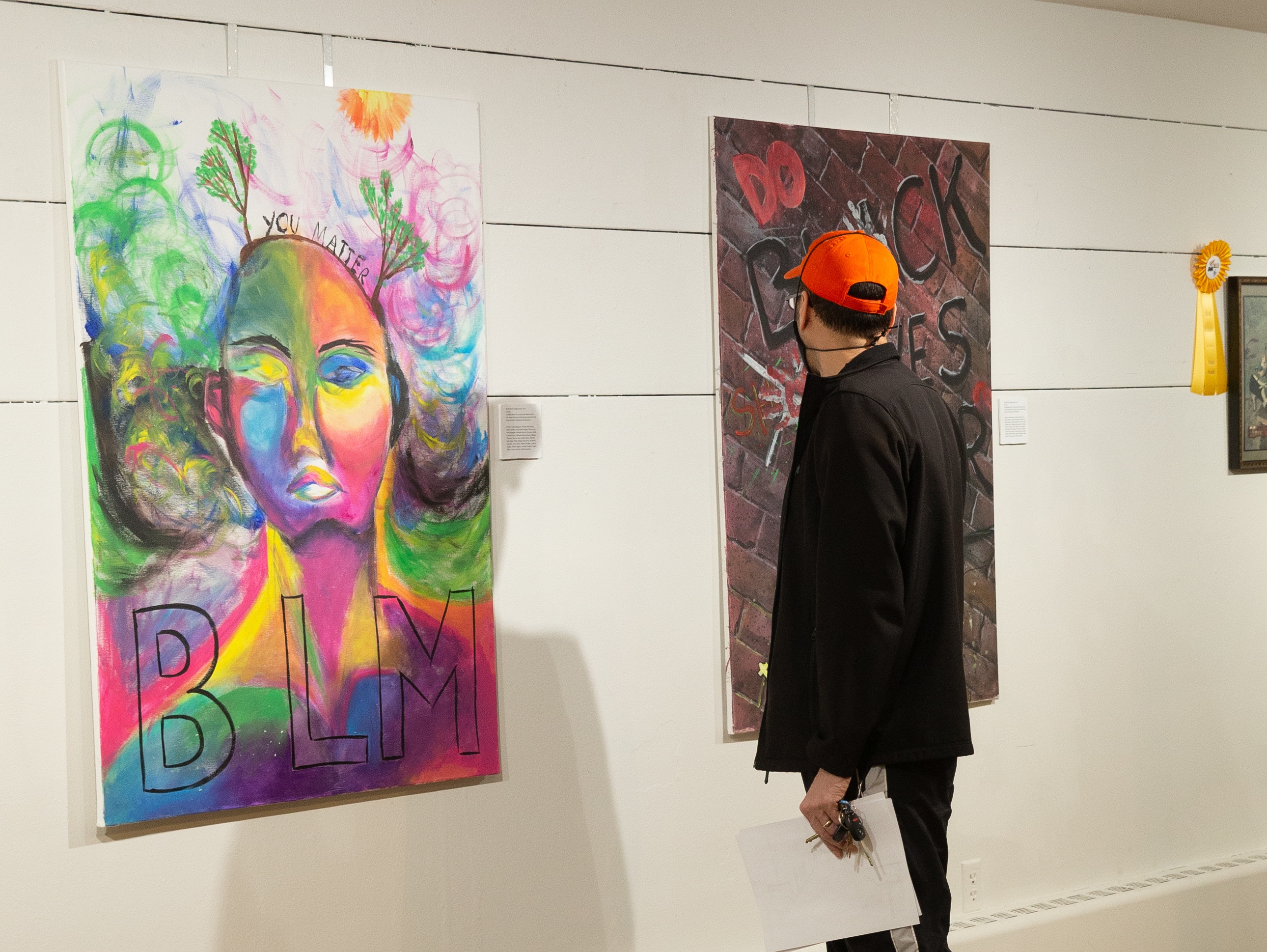 A person dressed in black with a orange baseball cap looking at an Art of Diversity painting