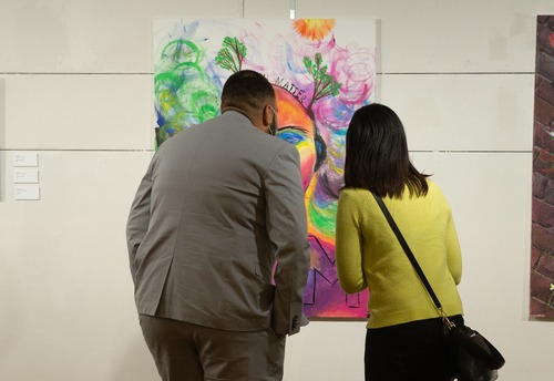 Two people one in a suit another in a lime green sweater looking at a painting