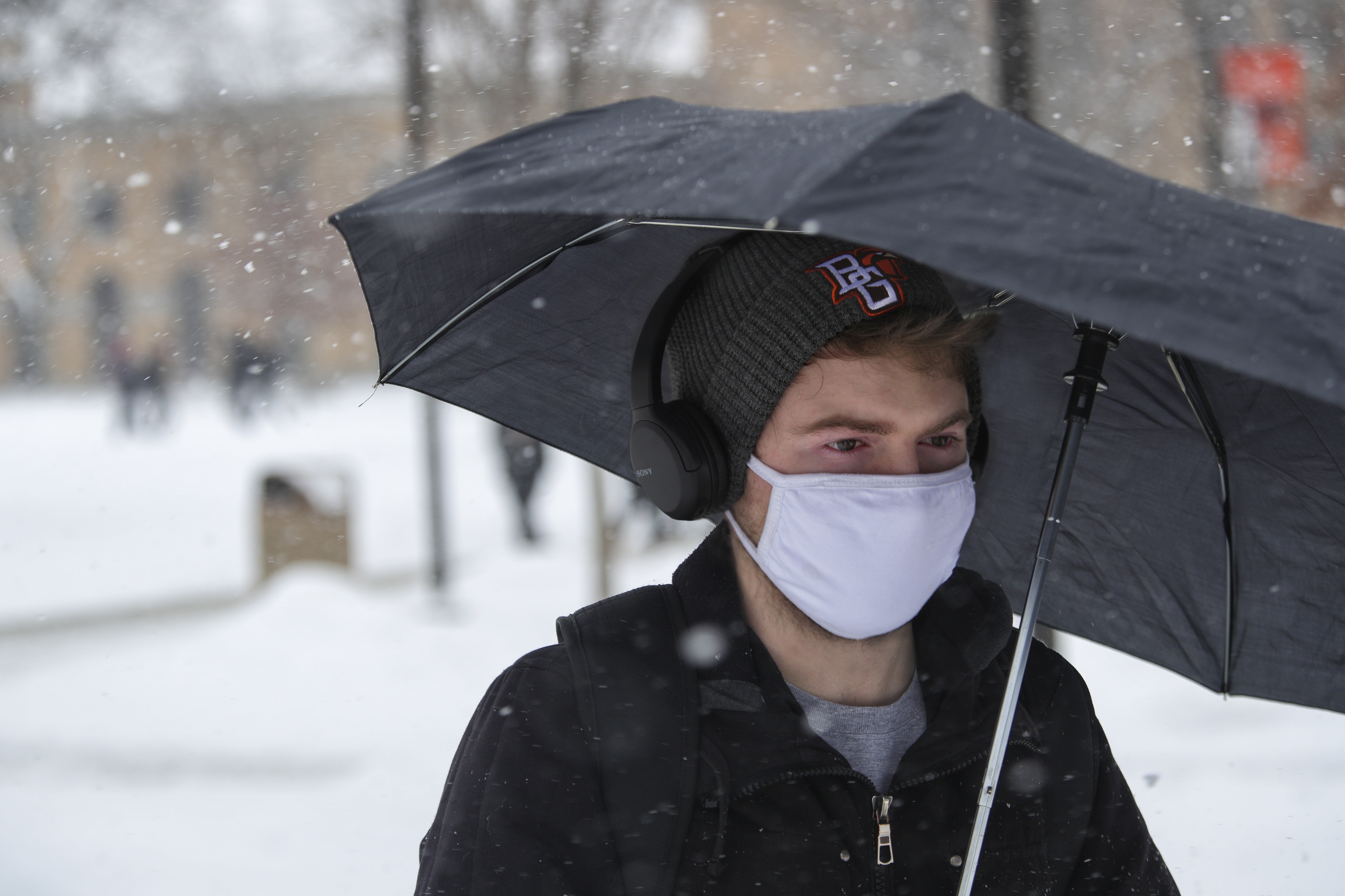 Trying to shield the snow, a student walks with an umbrella across campus. 