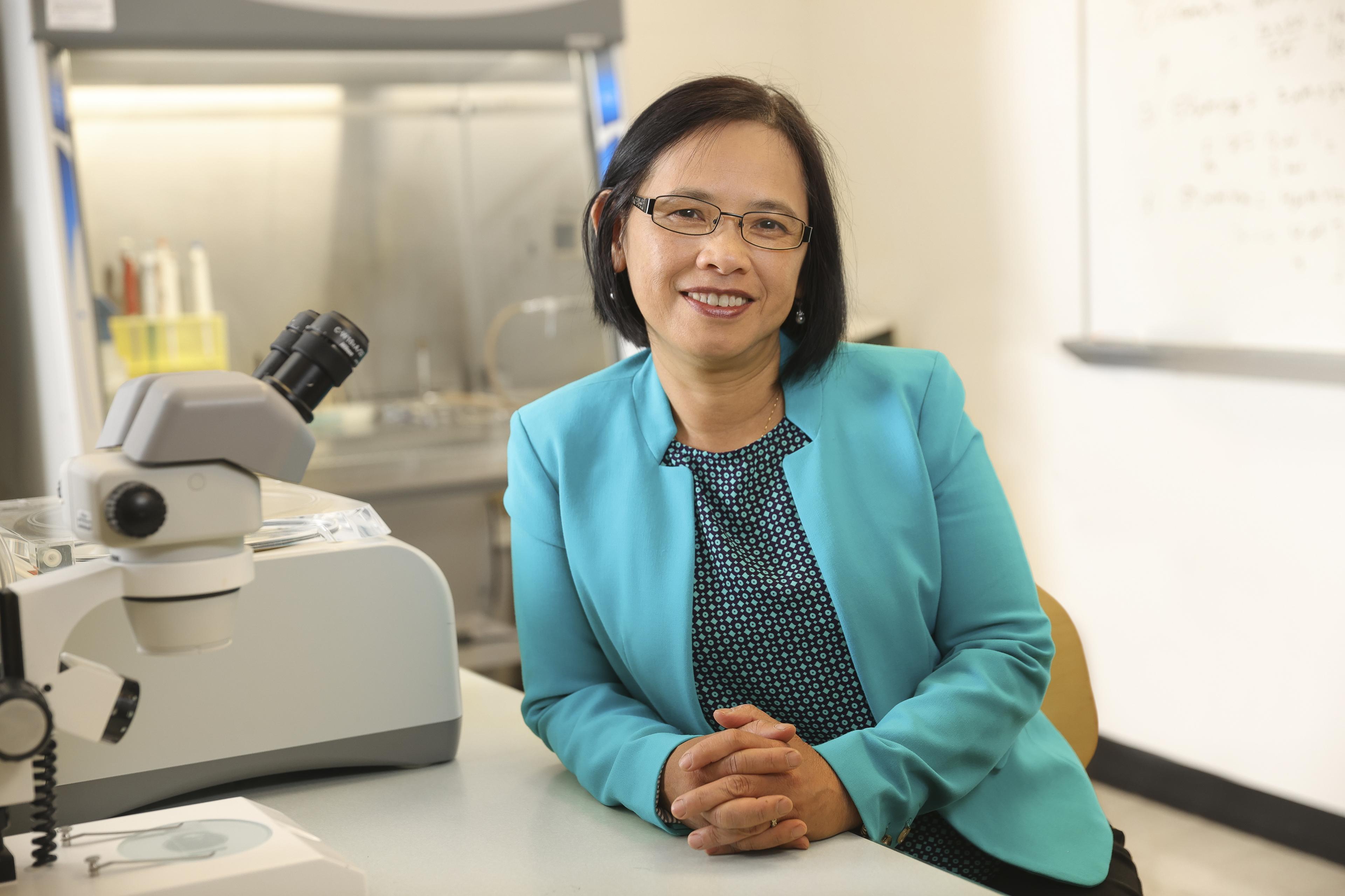 BGSU pathologist Dr. Vipa Phuntumart smiling in front of microscope