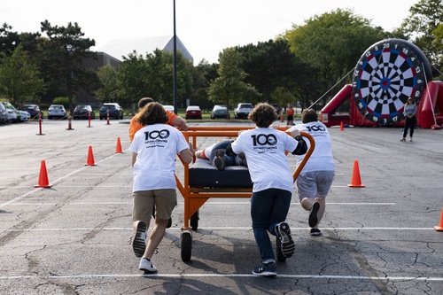 Four students push a rolling bed frame across a parking lot