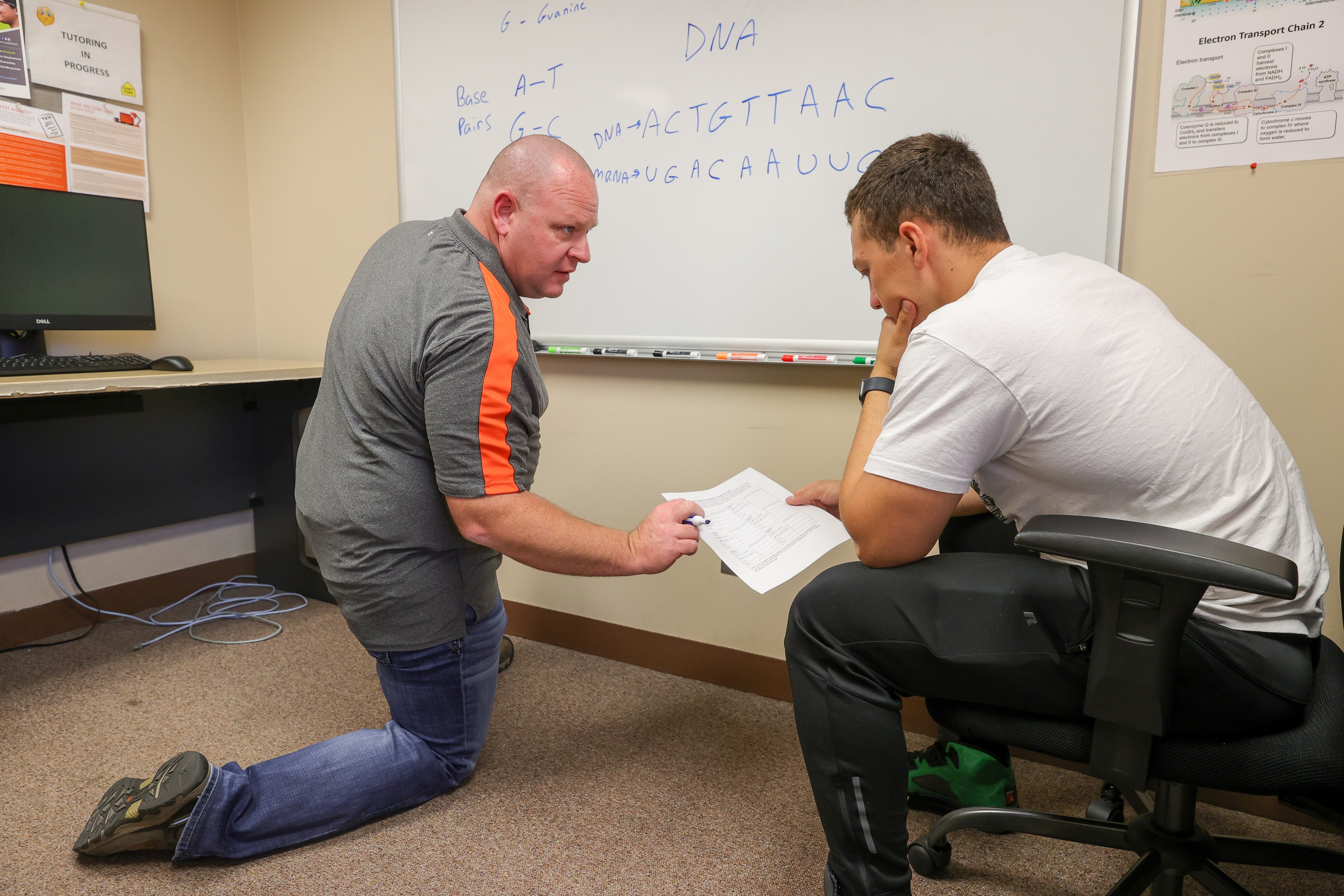 Jason Kaylor kneeling on one knee pointing at a paper someone is holding