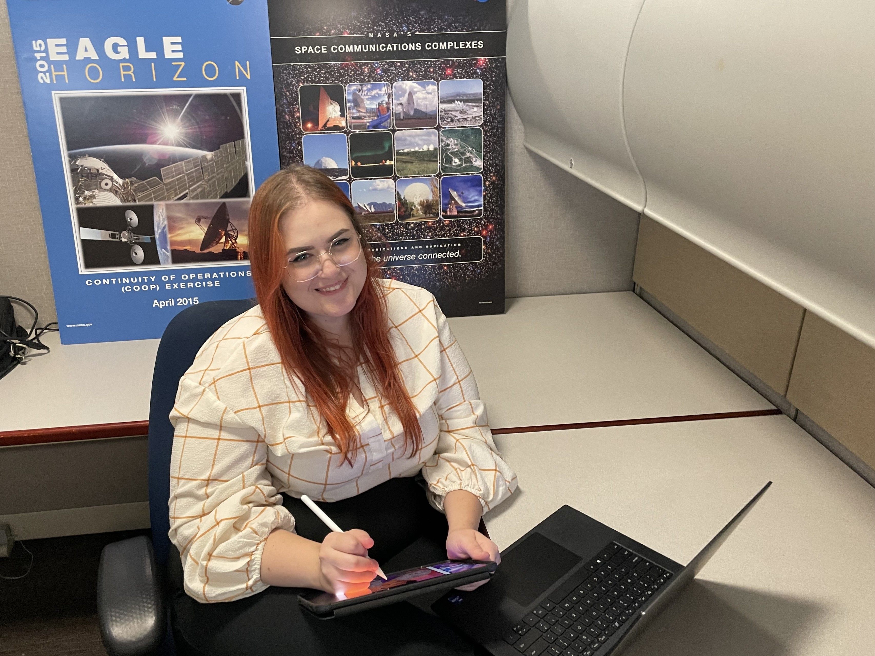 Heather Monaghan working on computer, while 2015 Eagle Horizon poster is behind her