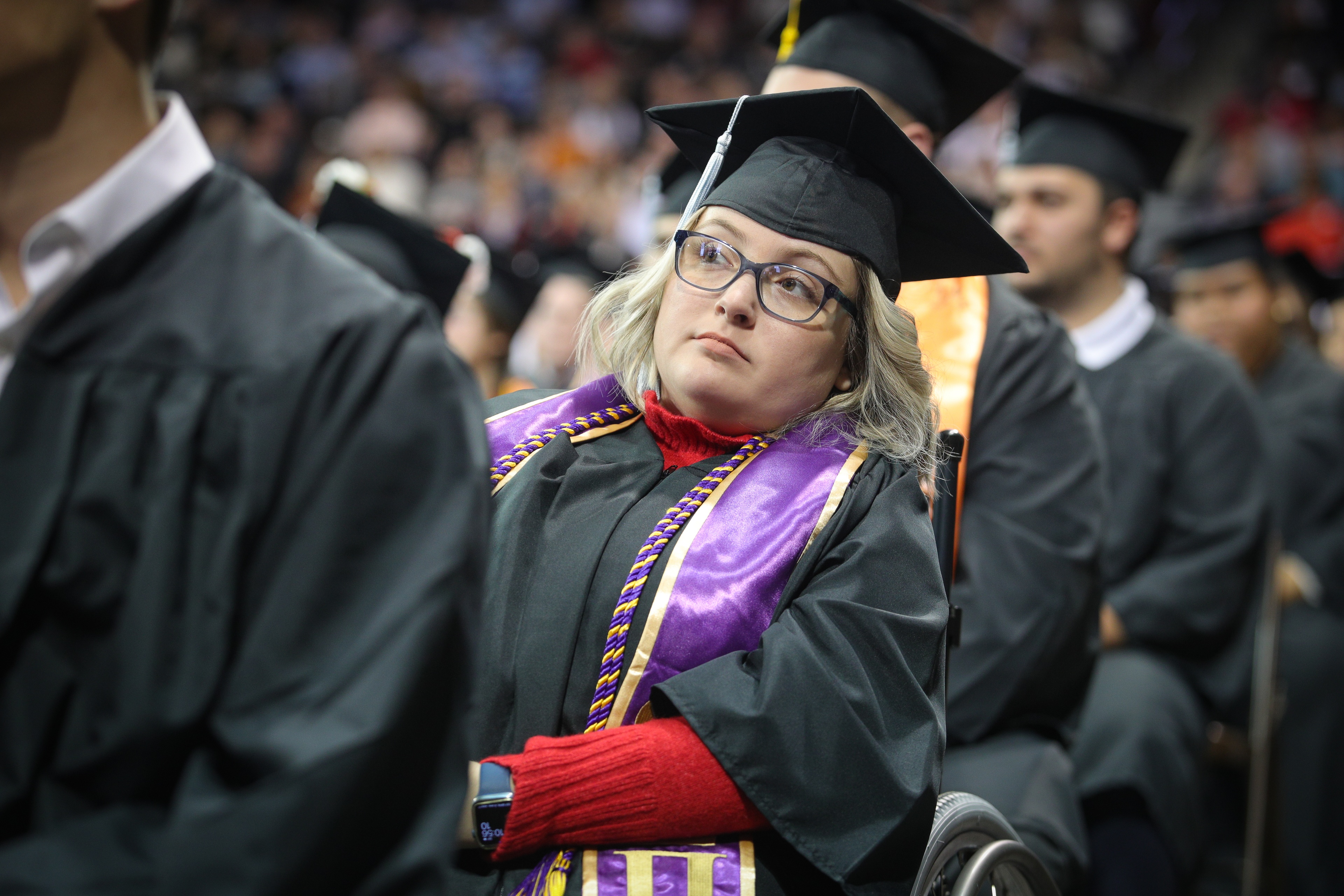 Female graduate sitting in a wheelchair looks at the Commencement speaker  