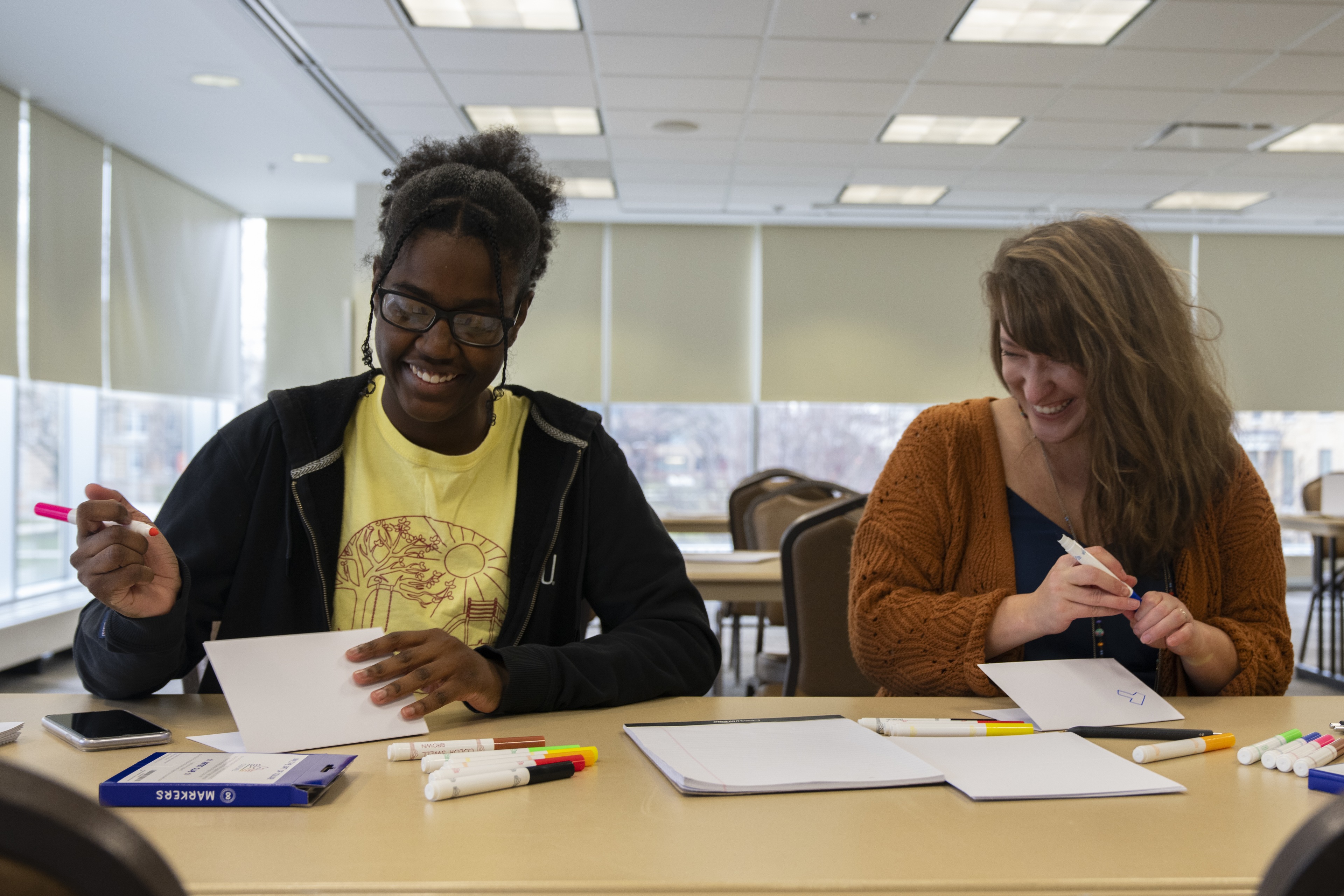 Two students smile while writing letters