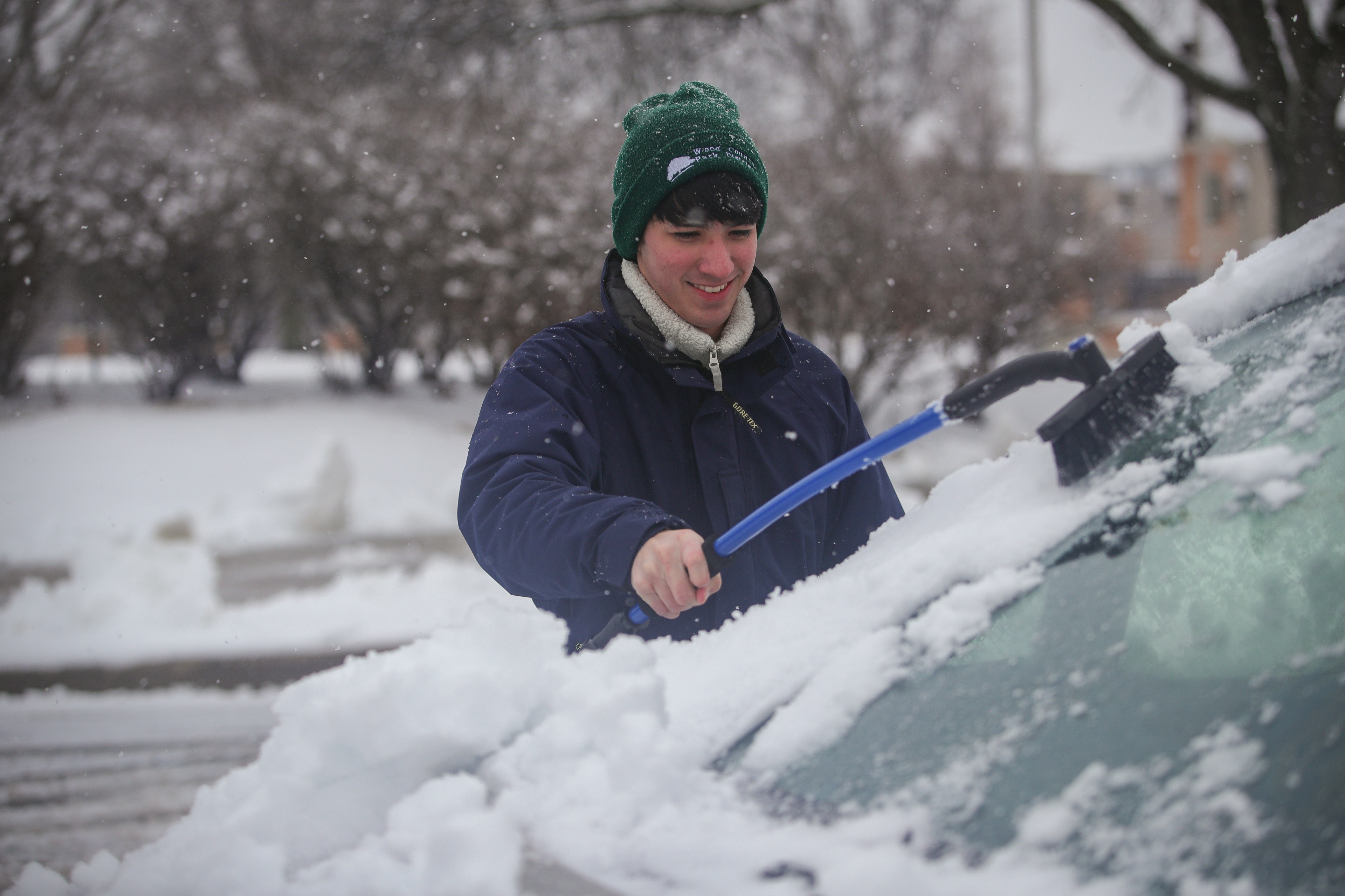 A person brushes snow off a vehicle windshield