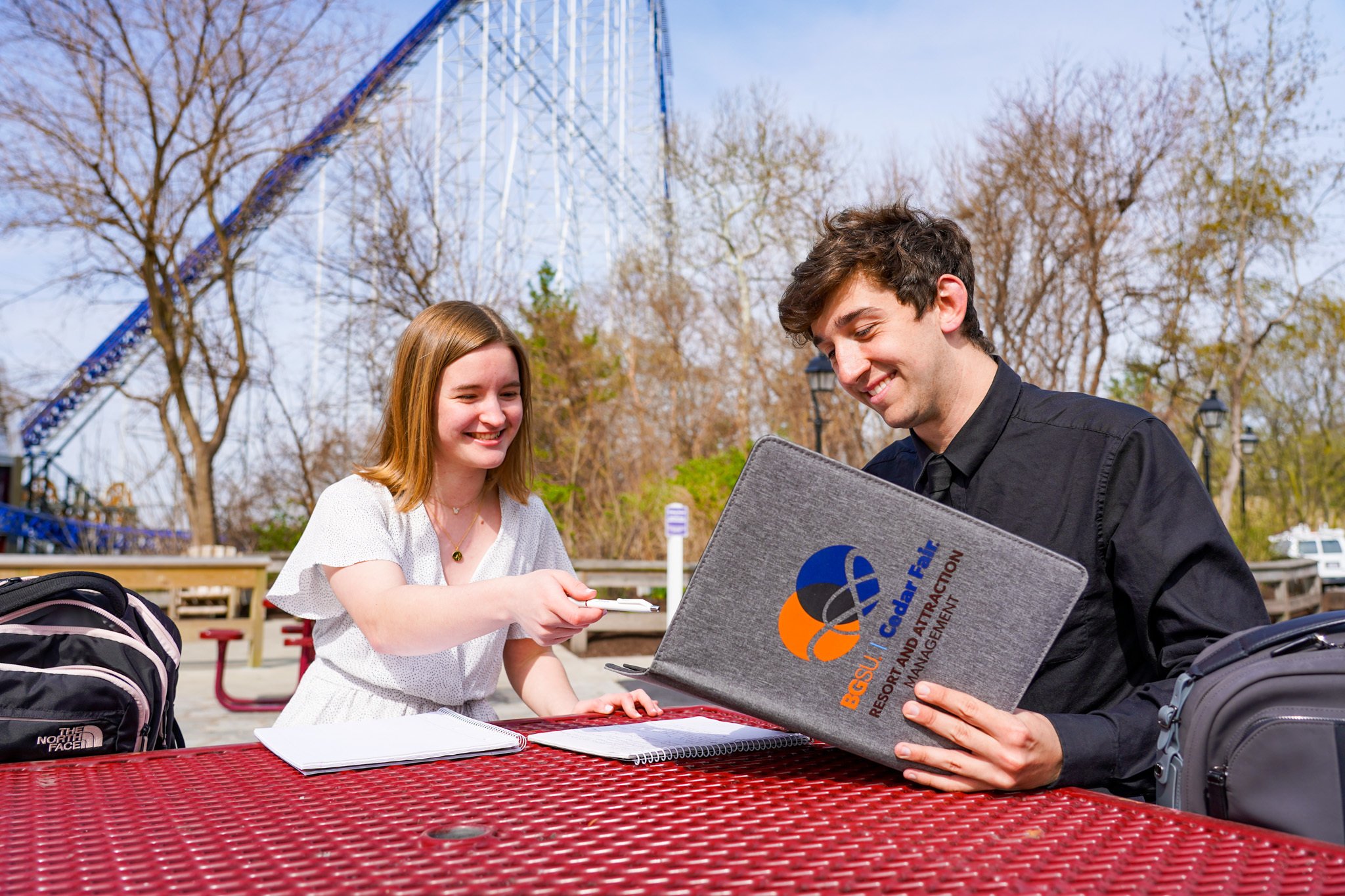 two students looking at a folder in front of a roller coaster