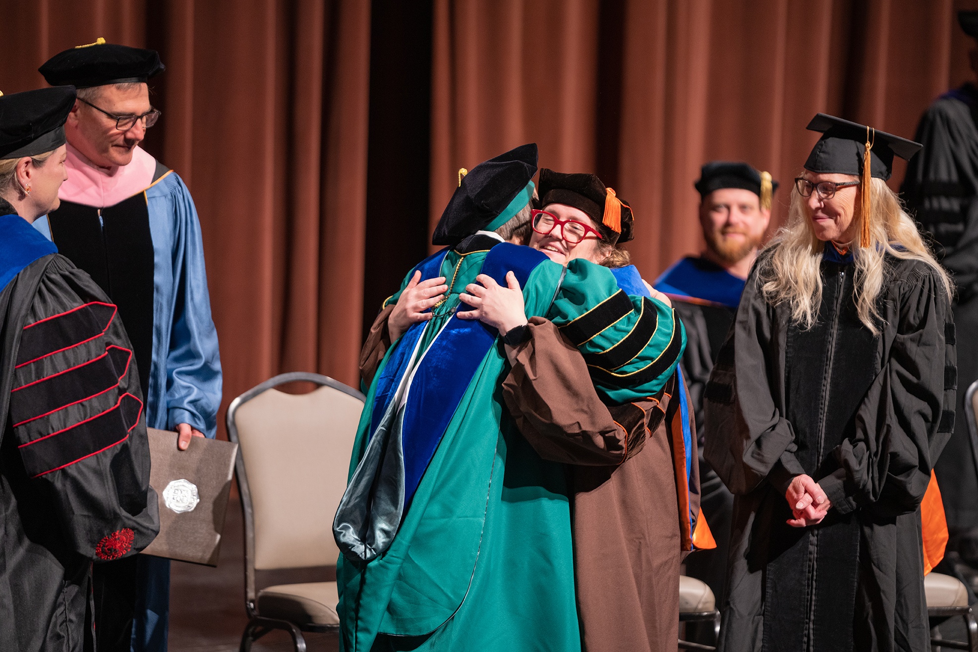 Doctoral candidate is hugged by dean at hooding ceremony