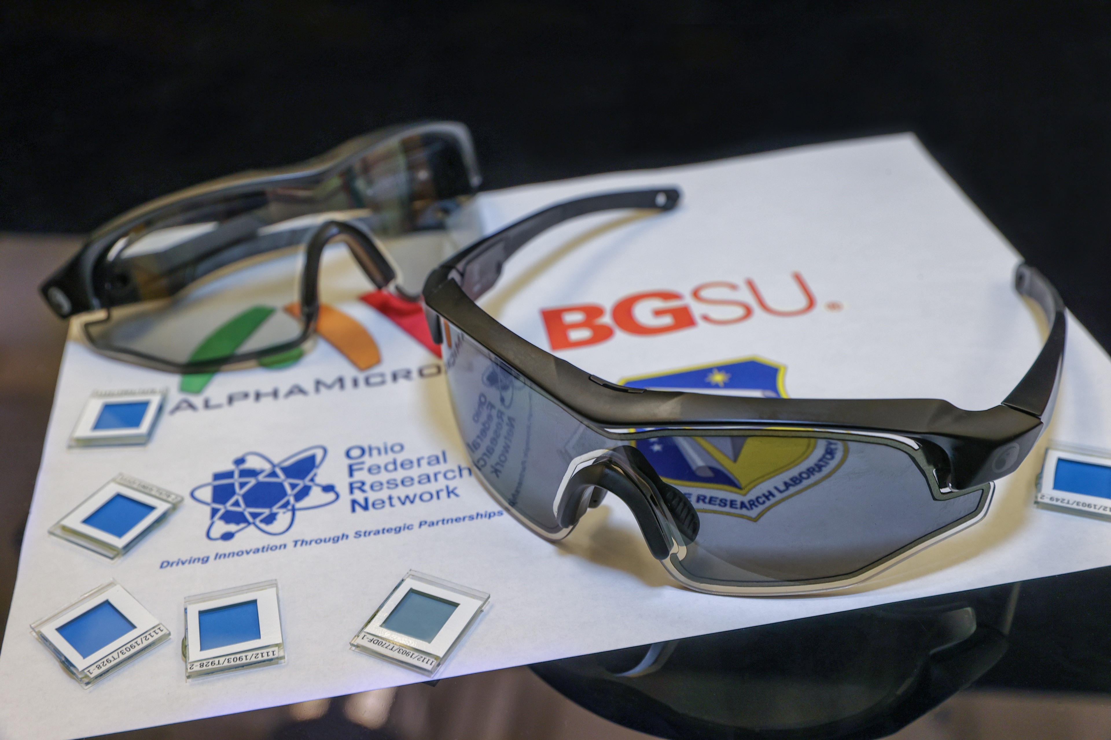 two pair of eyewear sitting on a paper with logos of BGSU, AlphaMicron, Ohio Federal Research Network, Air Force Research Laboratory 