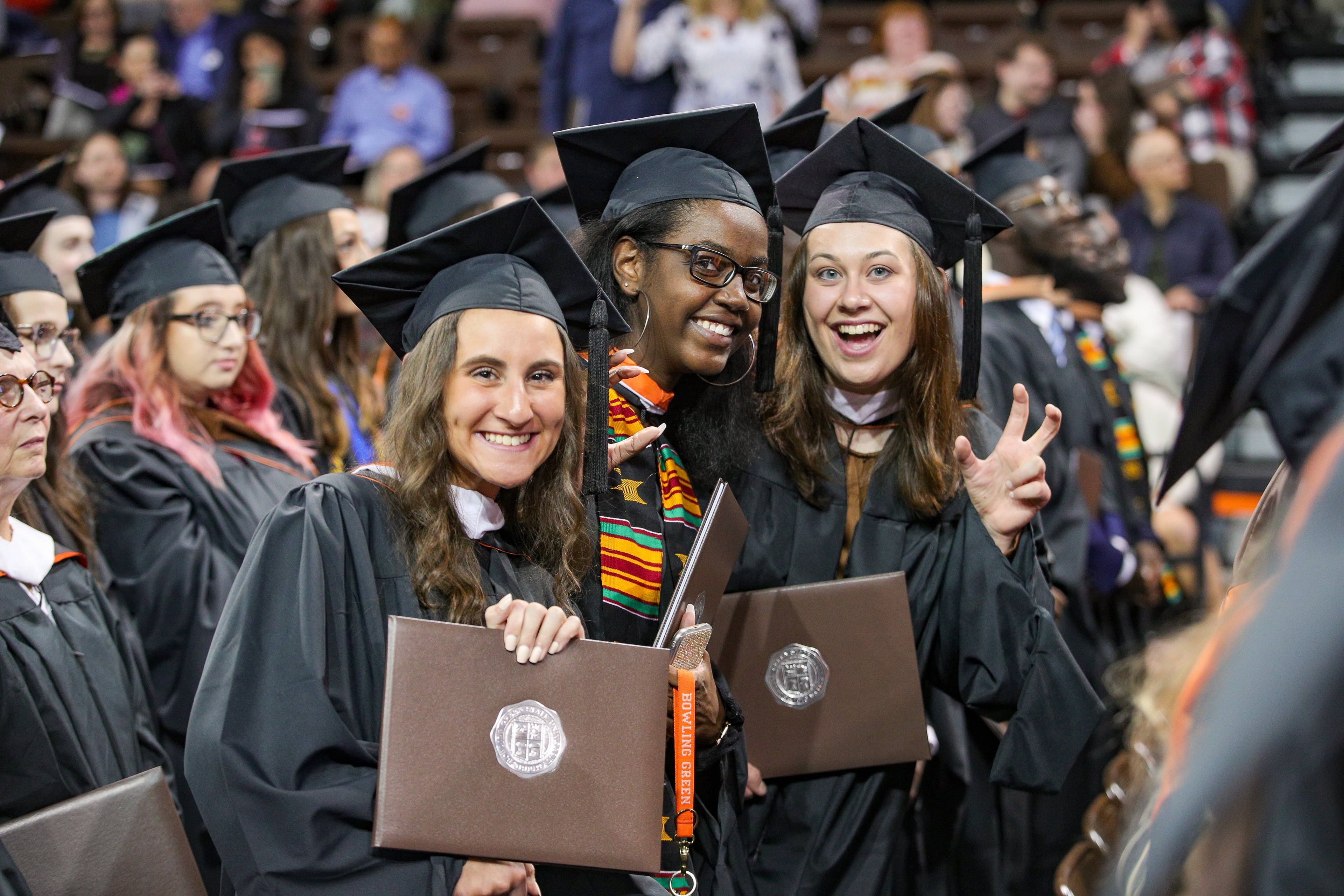 Three BGSU graduates show their diploma covers and give talons up sign
