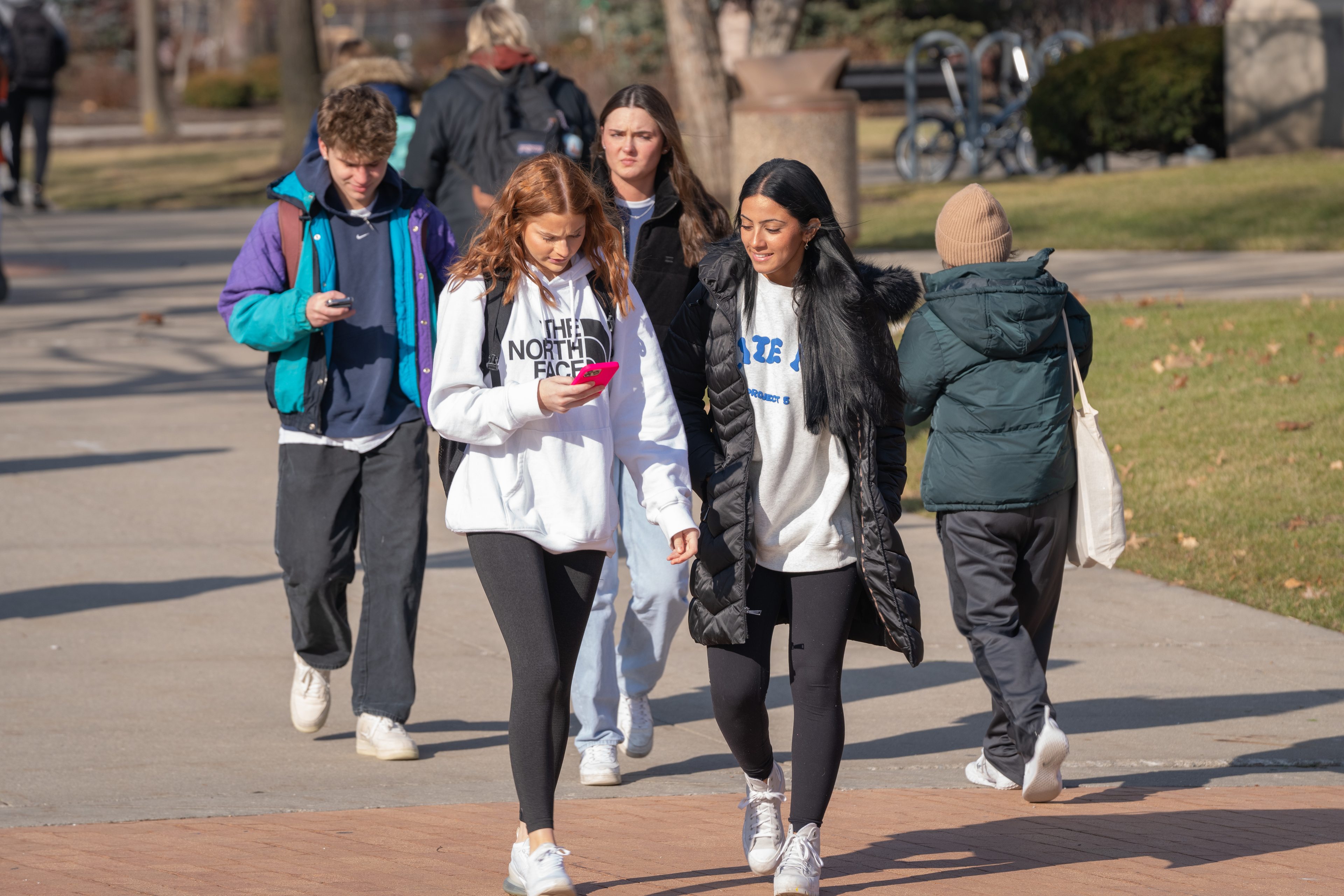 Students walk on BGSU campus looking at phones