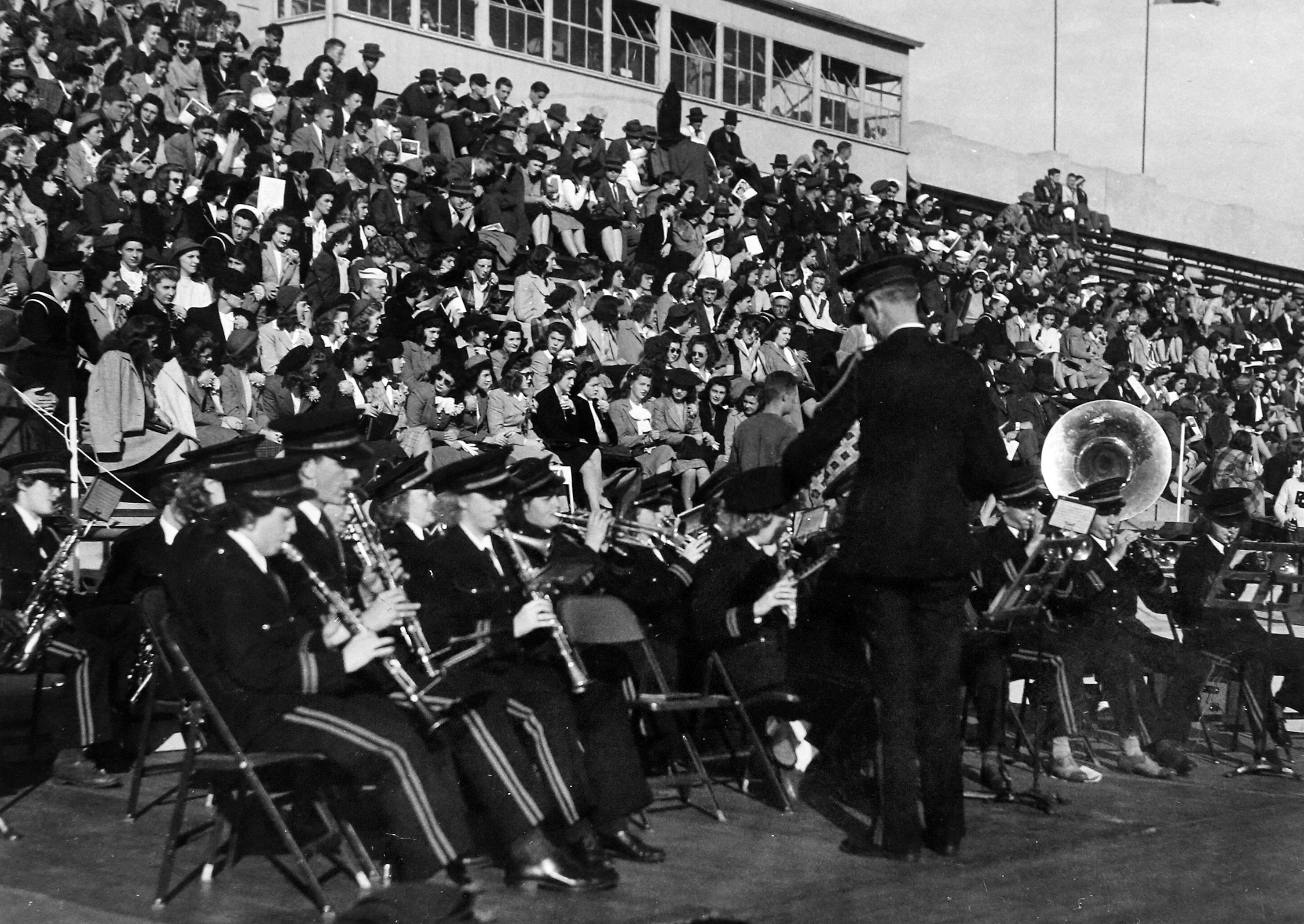Historic photo shows members of the BGSU band seated and playing at Doyt L. Perry Stadium in 1944 while fans fill the stands above them.