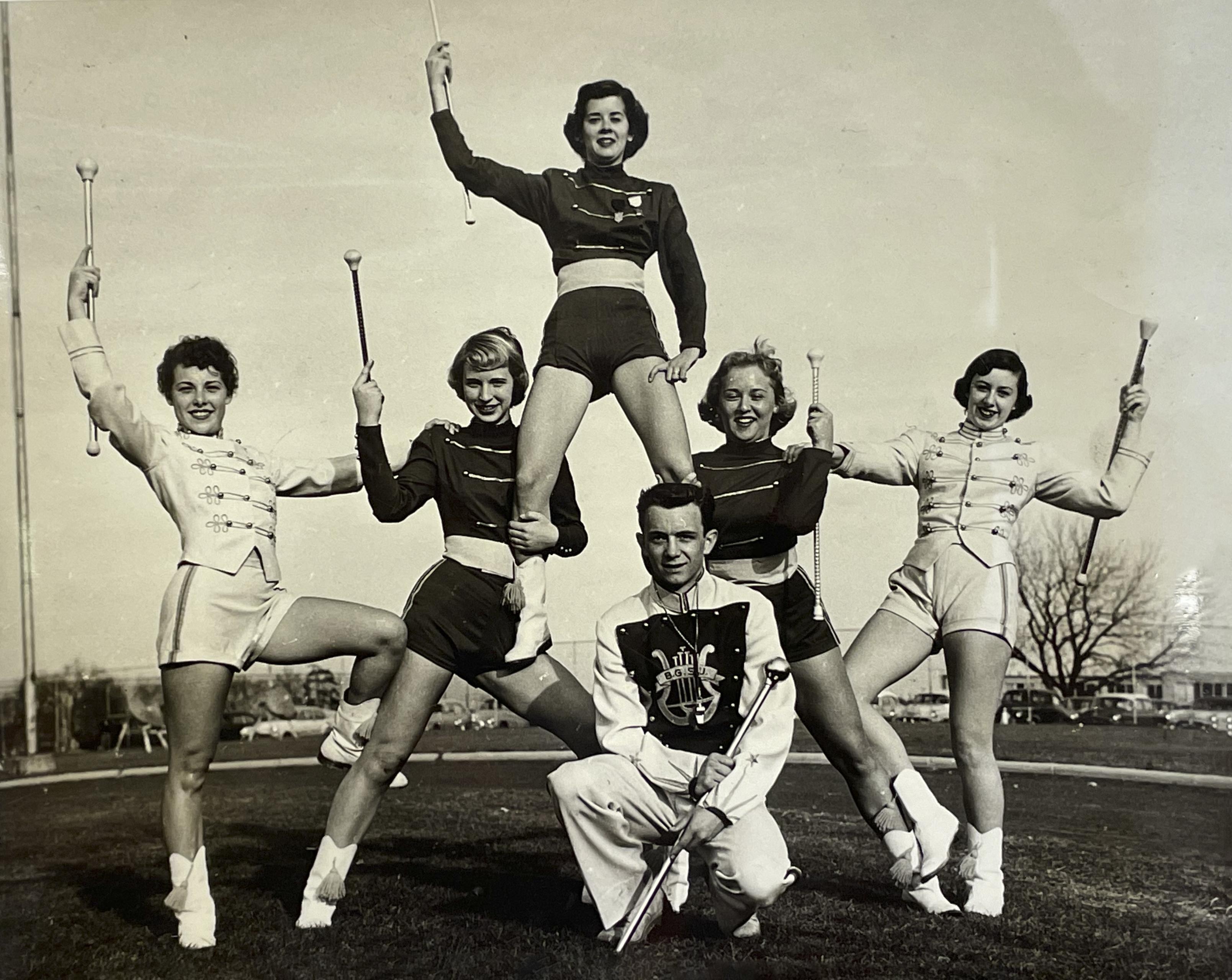 Five majorettes and a drum major pose in a pyramid formation