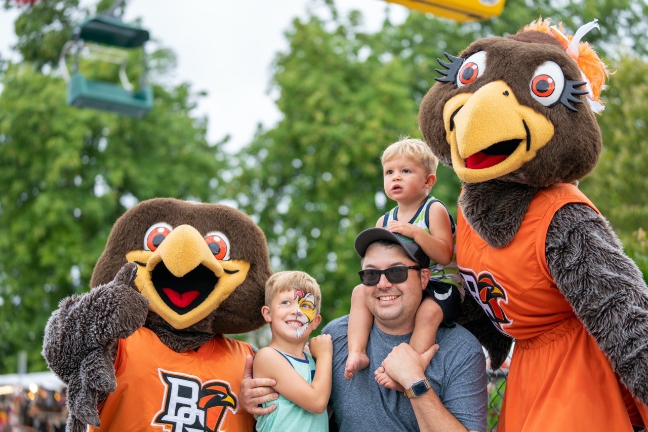 Two small children and an adult male smile with BGSU mascots Freddie and Frieda Falcon at the Ohio State Fair