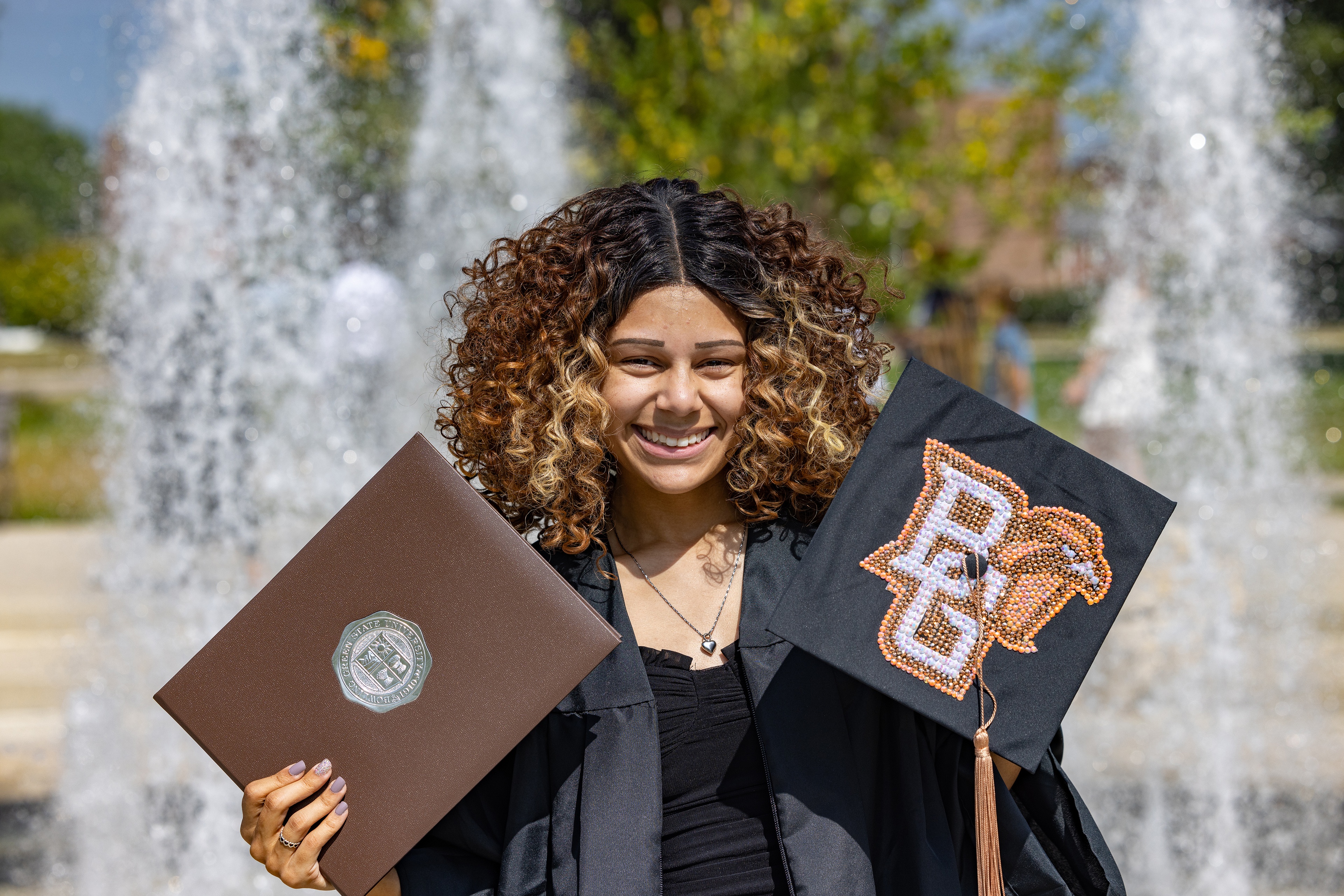 Graduate holds diploma cover and mortarboard  