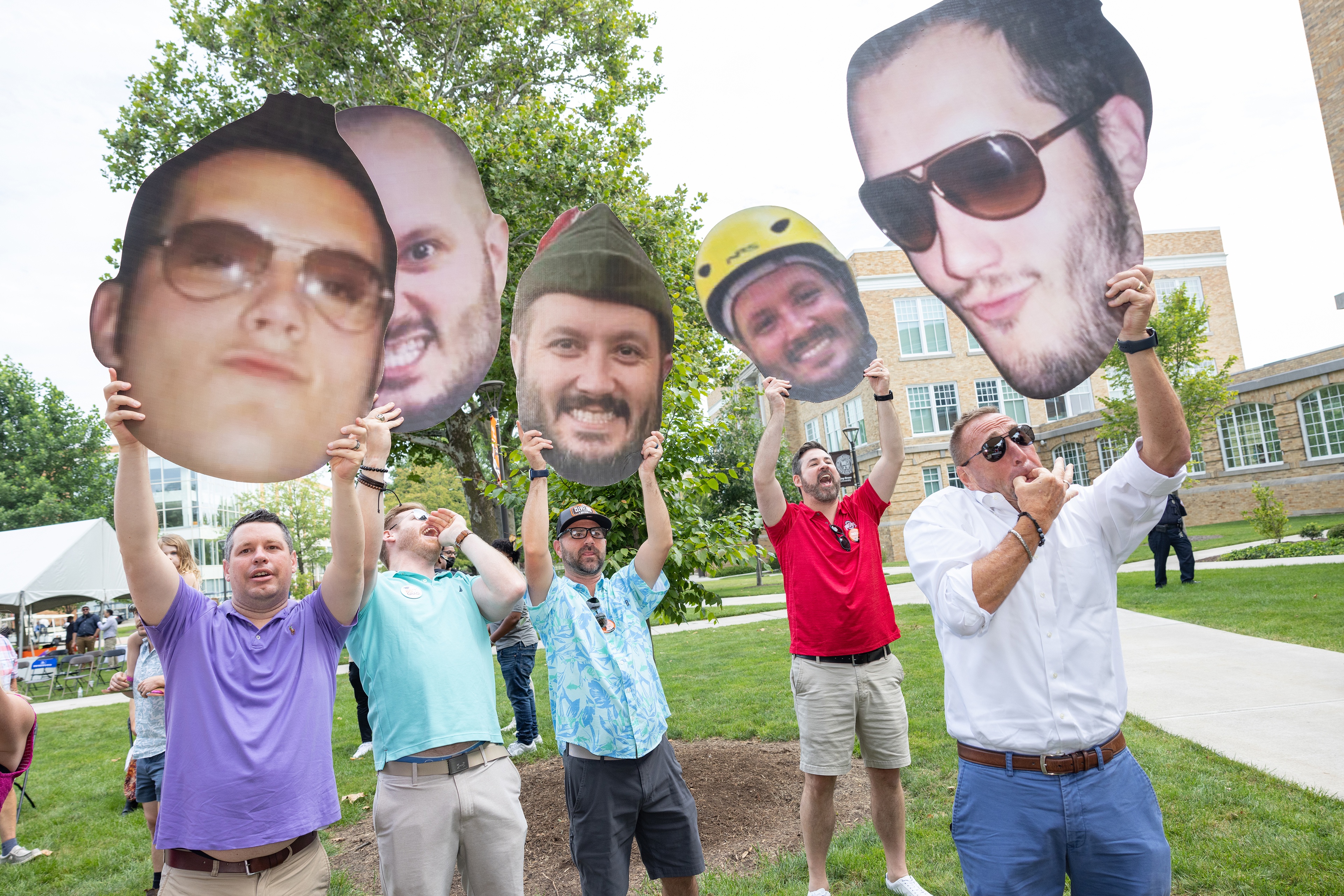 Four men hold up giant photos of their heads during graduation 