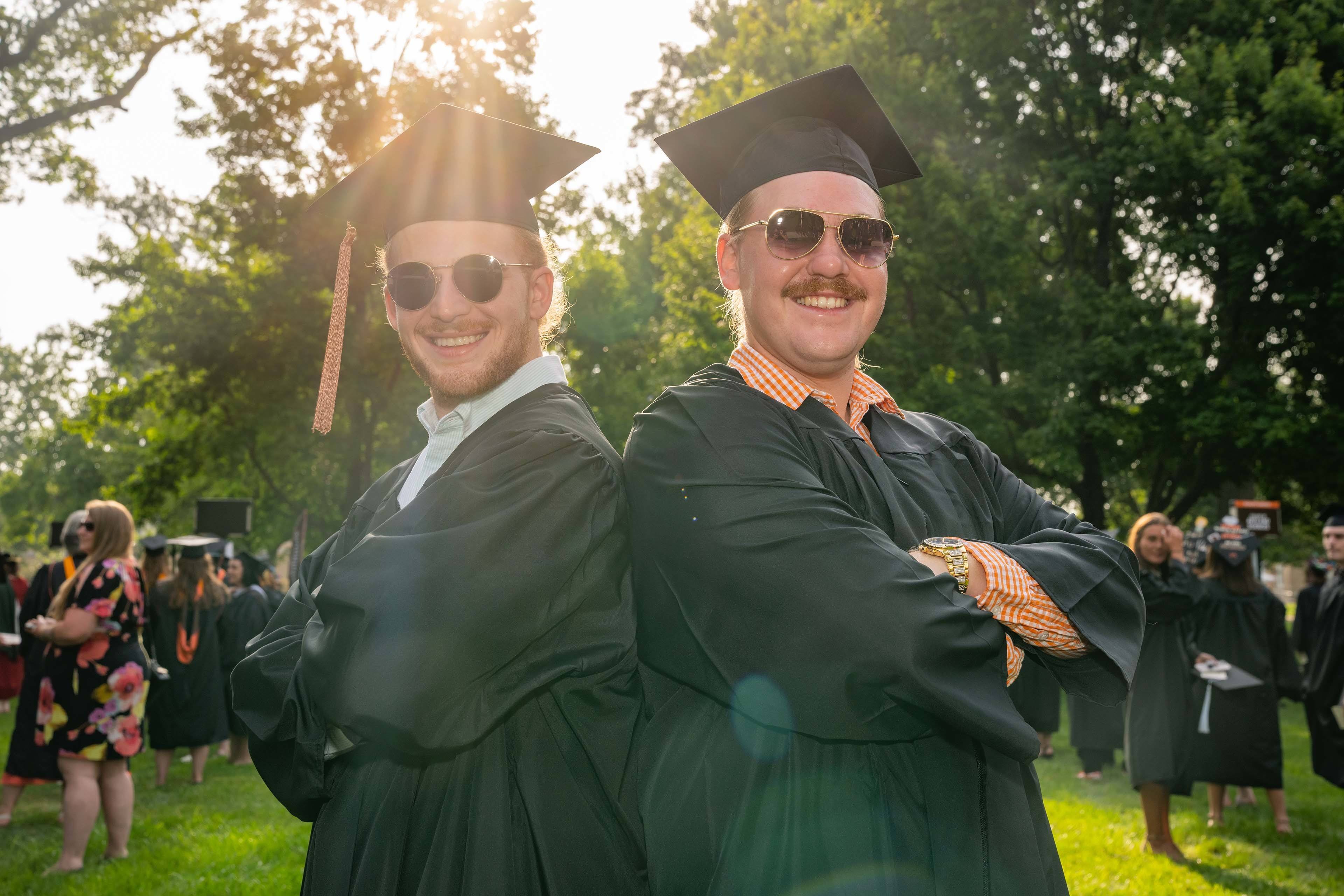 Two graduates pose back to back in sunglasses 