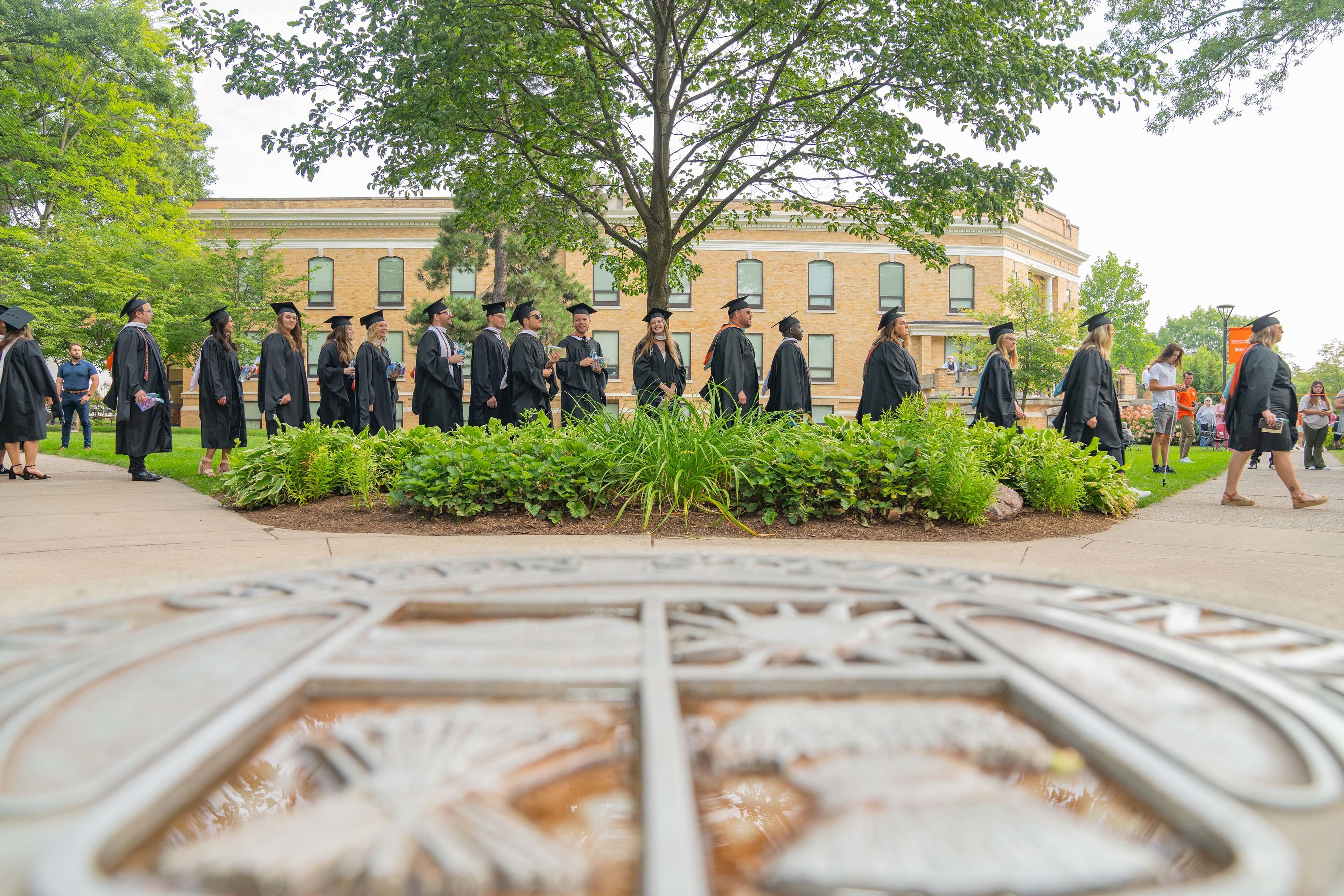 Graduates pass by the University Seal